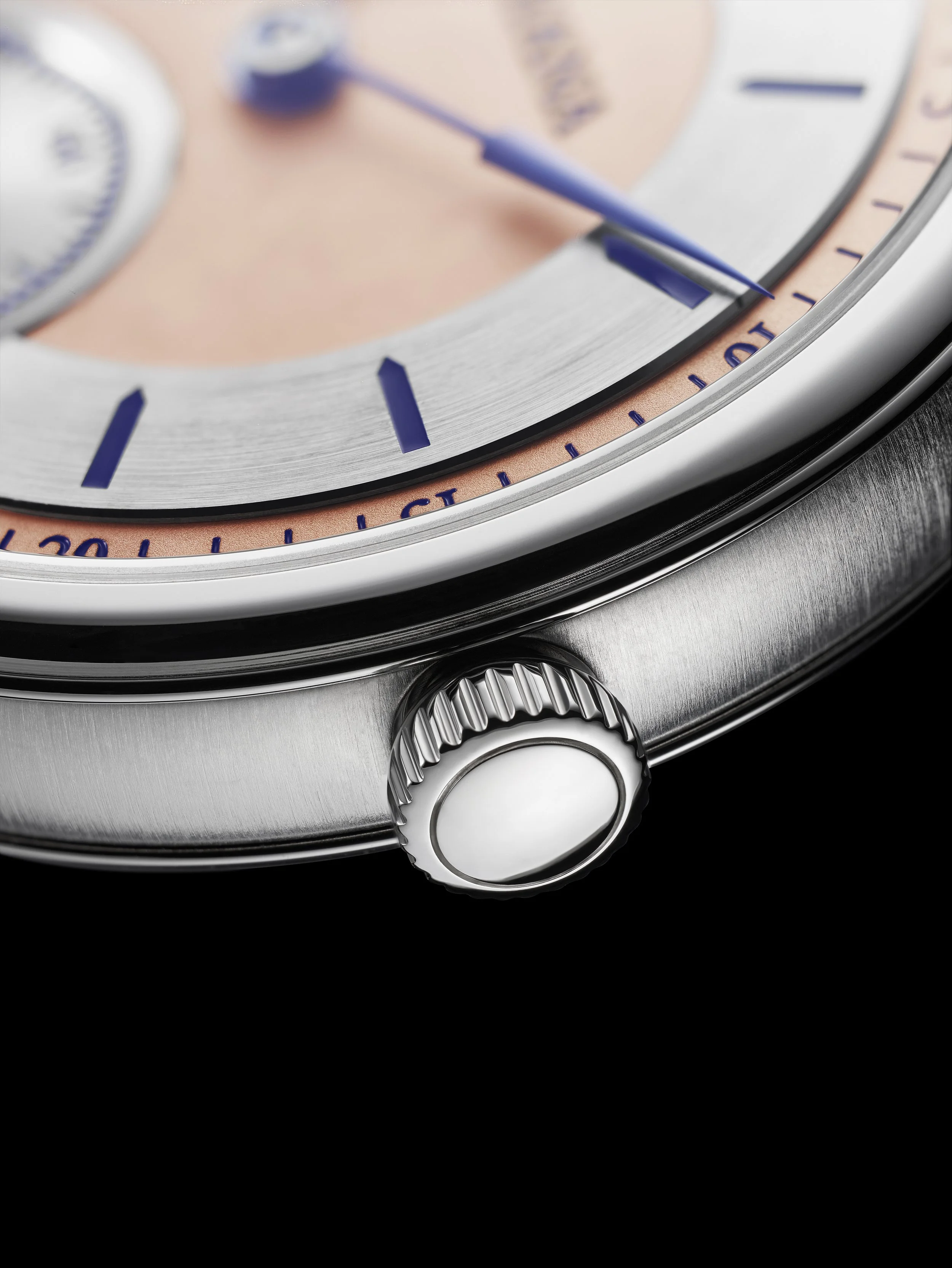 Close-up of a luxury wristwatch, showing the crown and part of the dial with pink and silver details.