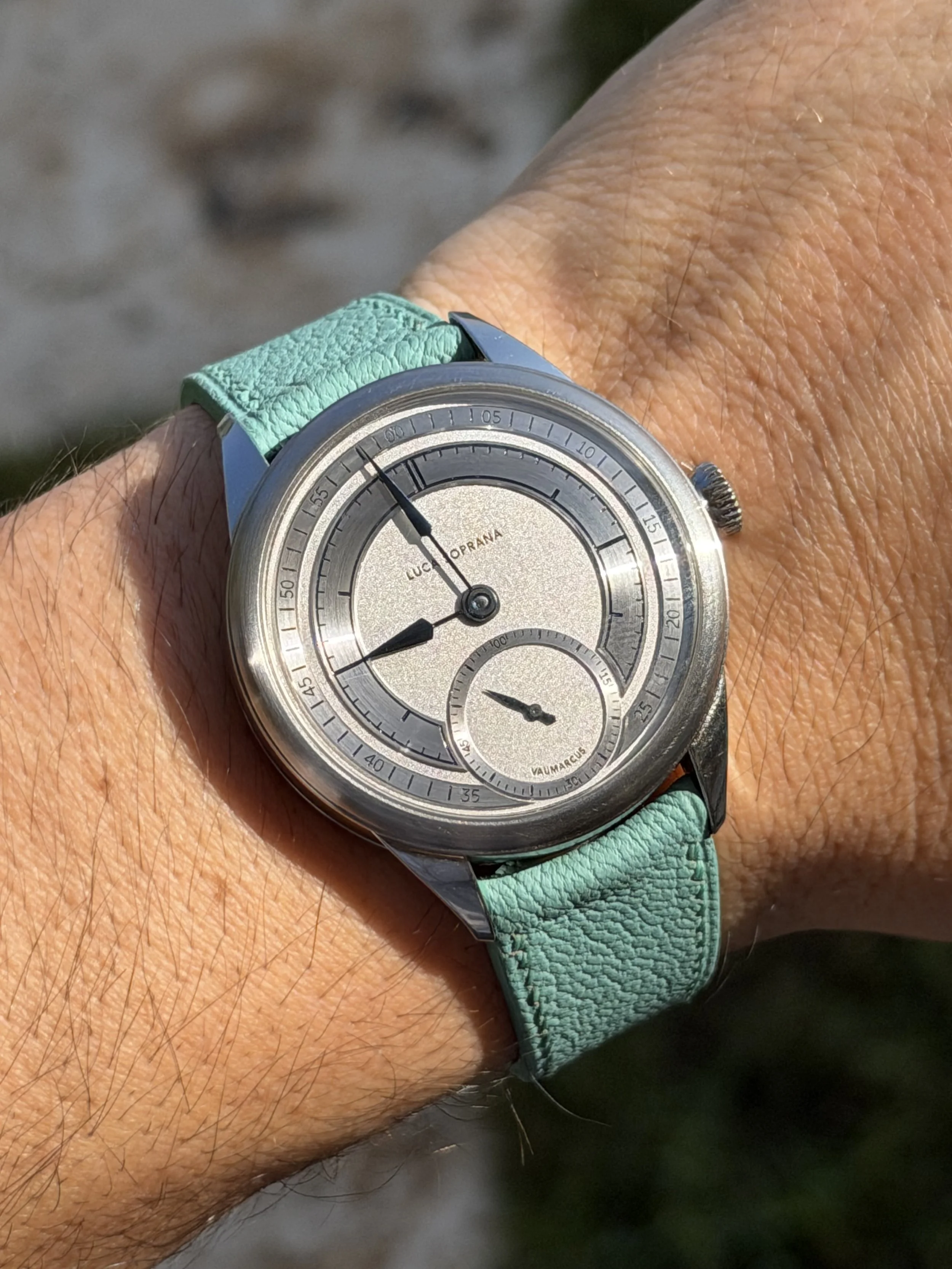 A wristwatch with a silver face, black hands, and a light green strap on a person's wrist.