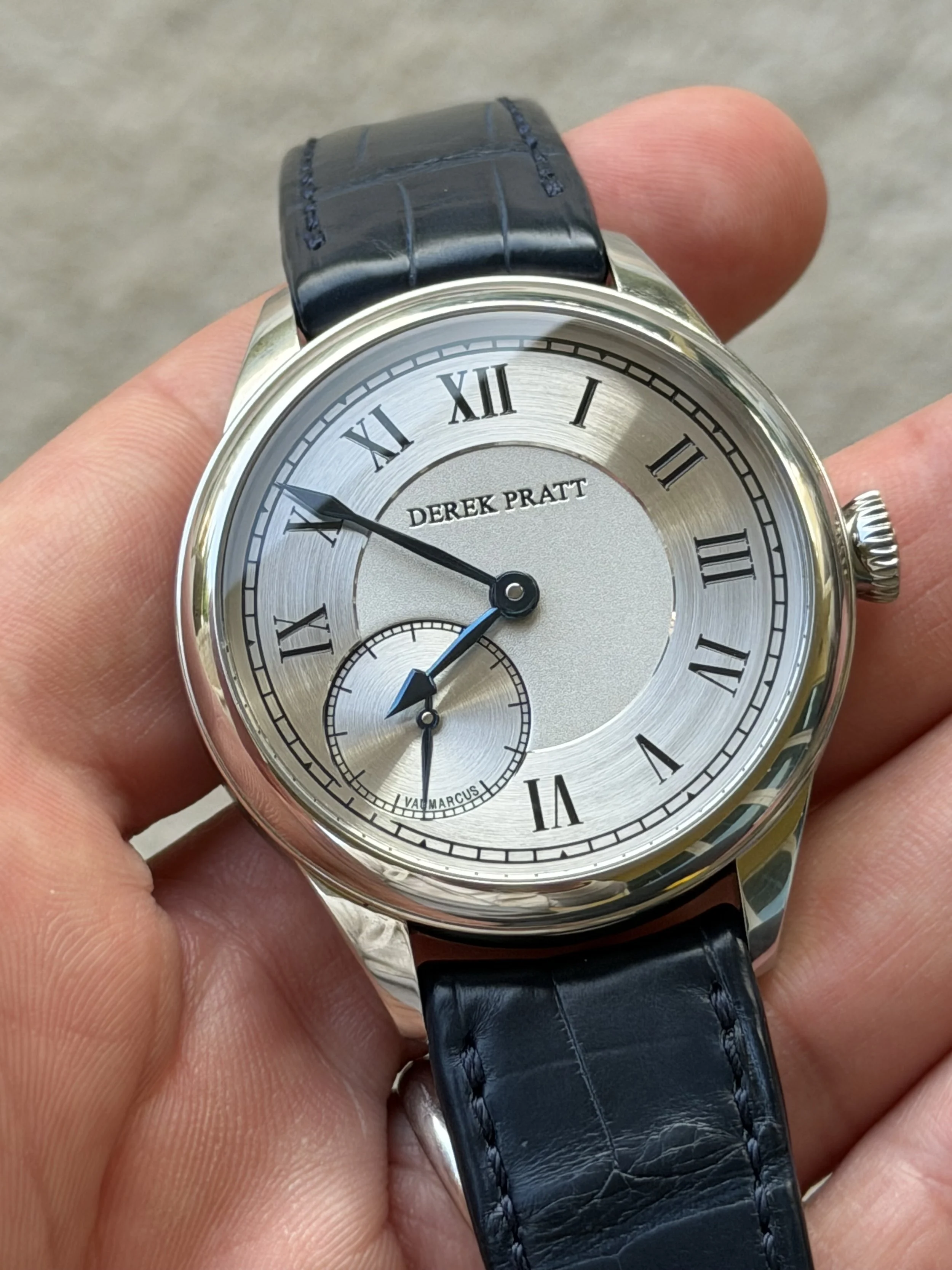 A wristwatch with a silver dial, black Roman numerals, and a black leather strap, displaying the time as approximately 8:52.