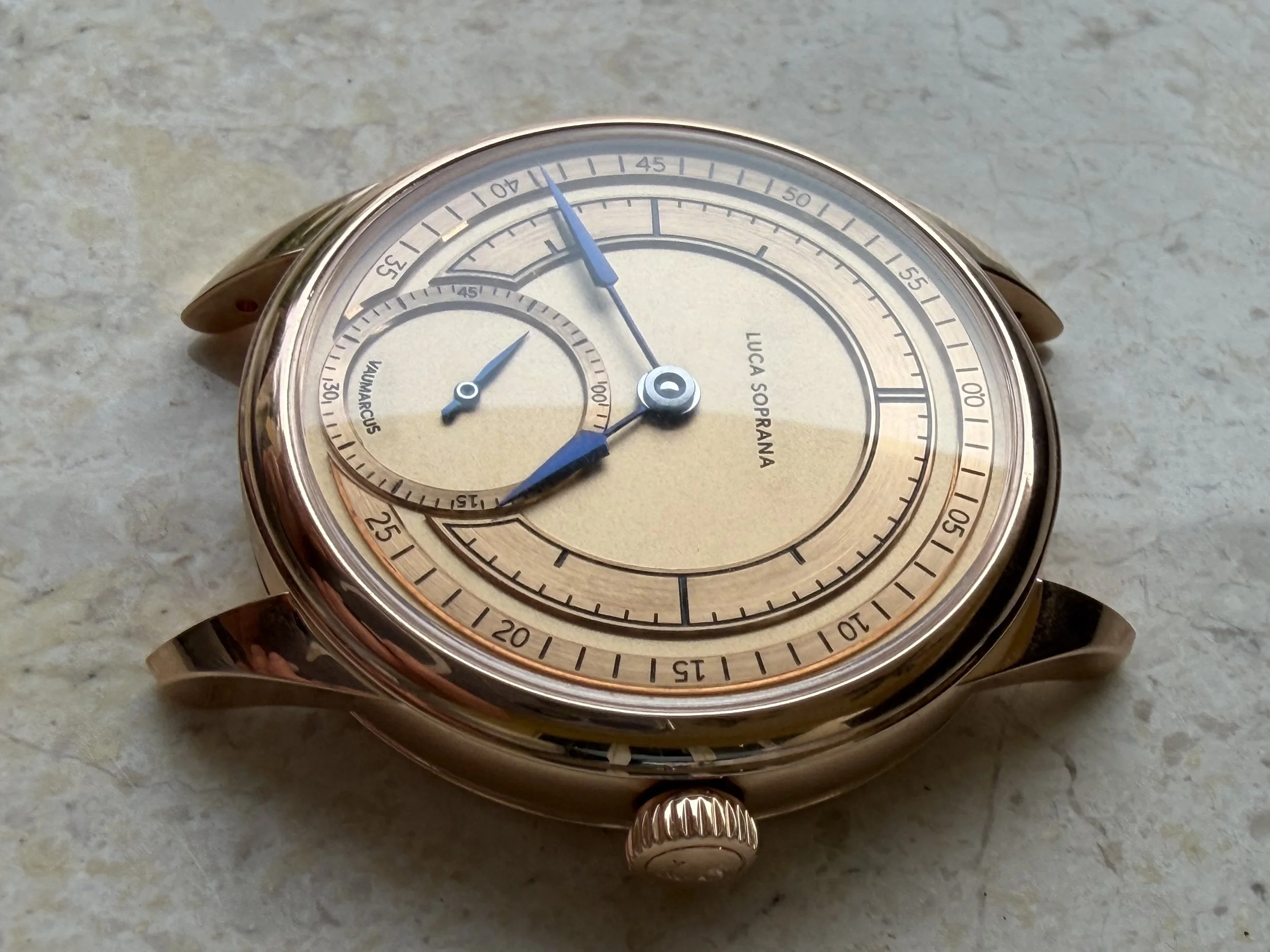 A gold-colored Luca Soprana wristwatch with a dual dial and multiple hands, resting on a textured light-colored surface.