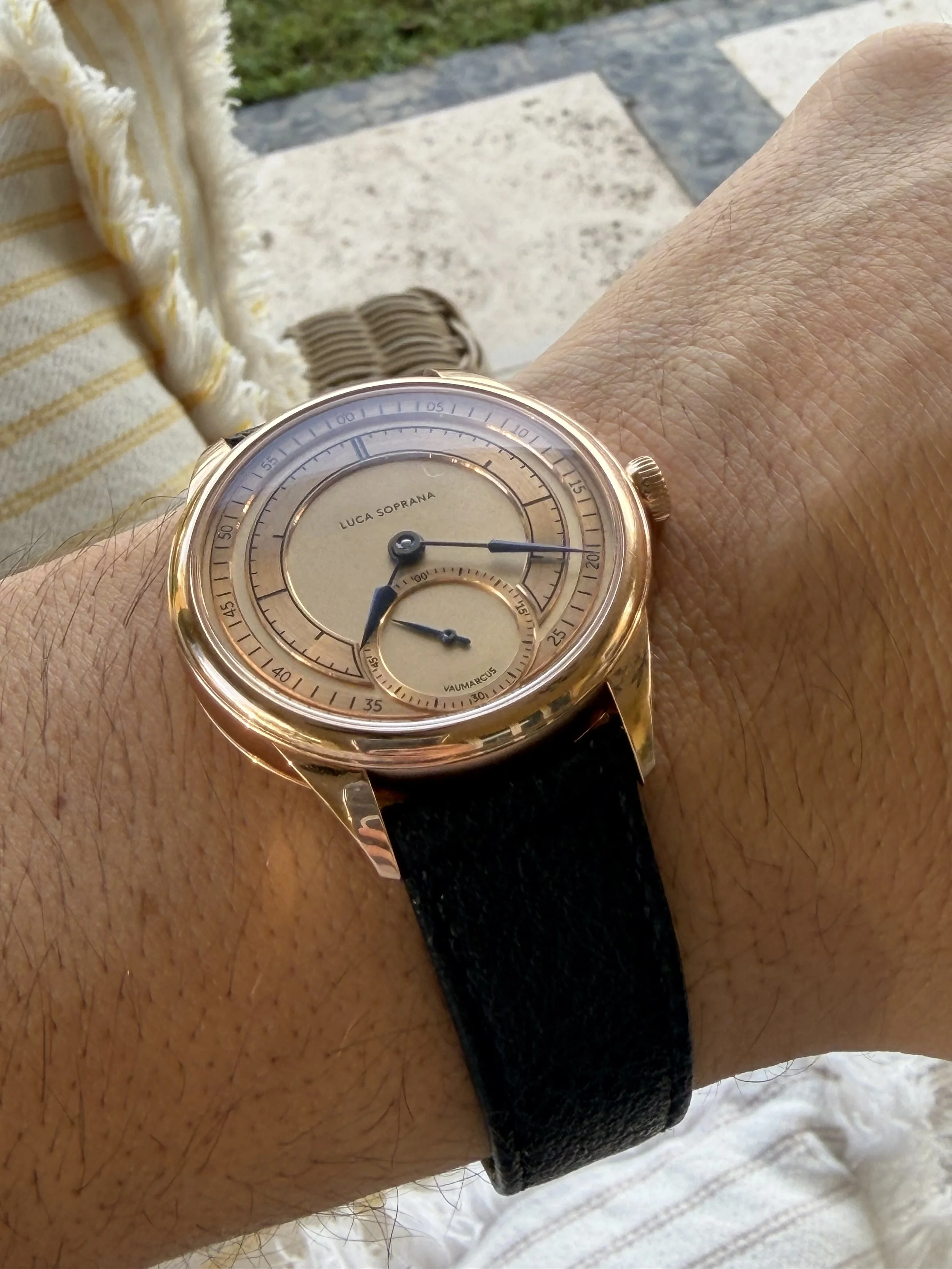 A wristwatch with a gold case and black leather strap showing the time, worn on a person's wrist outdoors.