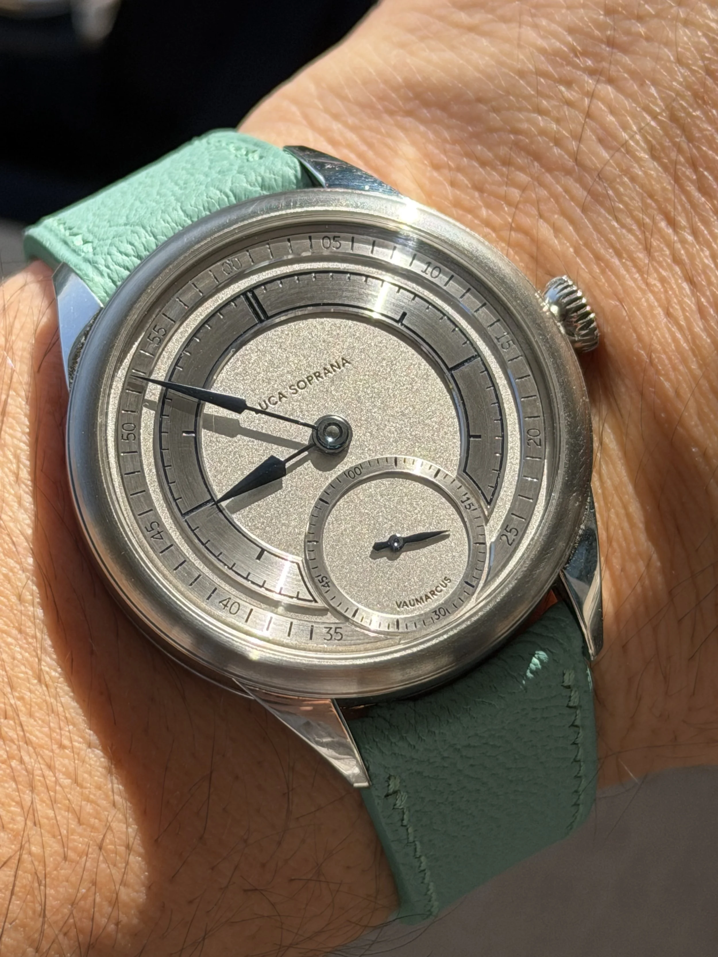 A wristwatch with a silver face, black and silver hands, and a mint green strap on a person's wrist.