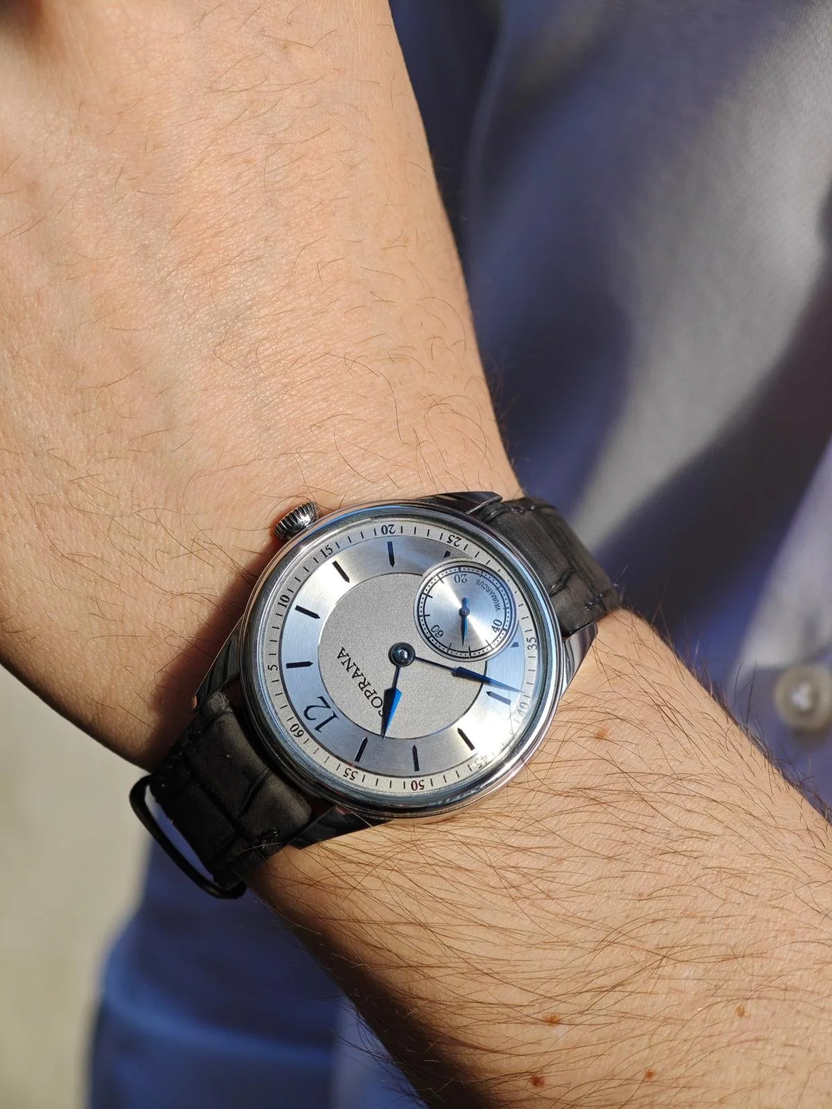 A wristwatch on a person's wrist, showing the time as 2:53 with a black leather strap and a silver dial.