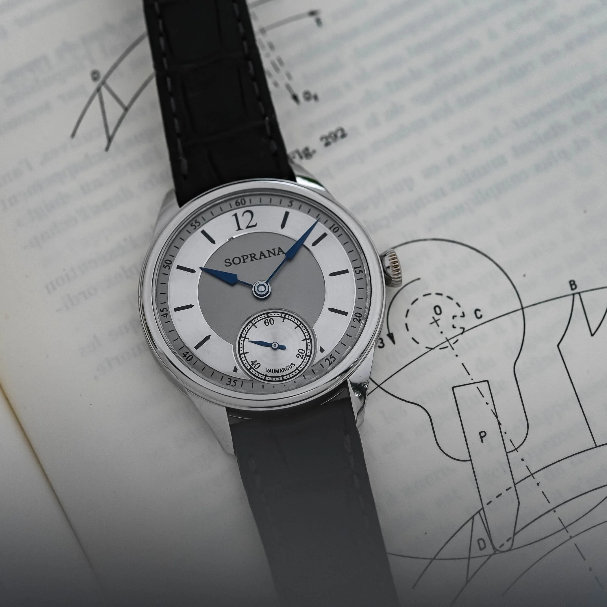 A silver wristwatch with a grey dial, black leather strap, and the brand name Soprana, resting on a technical drawing of a mechanical device.