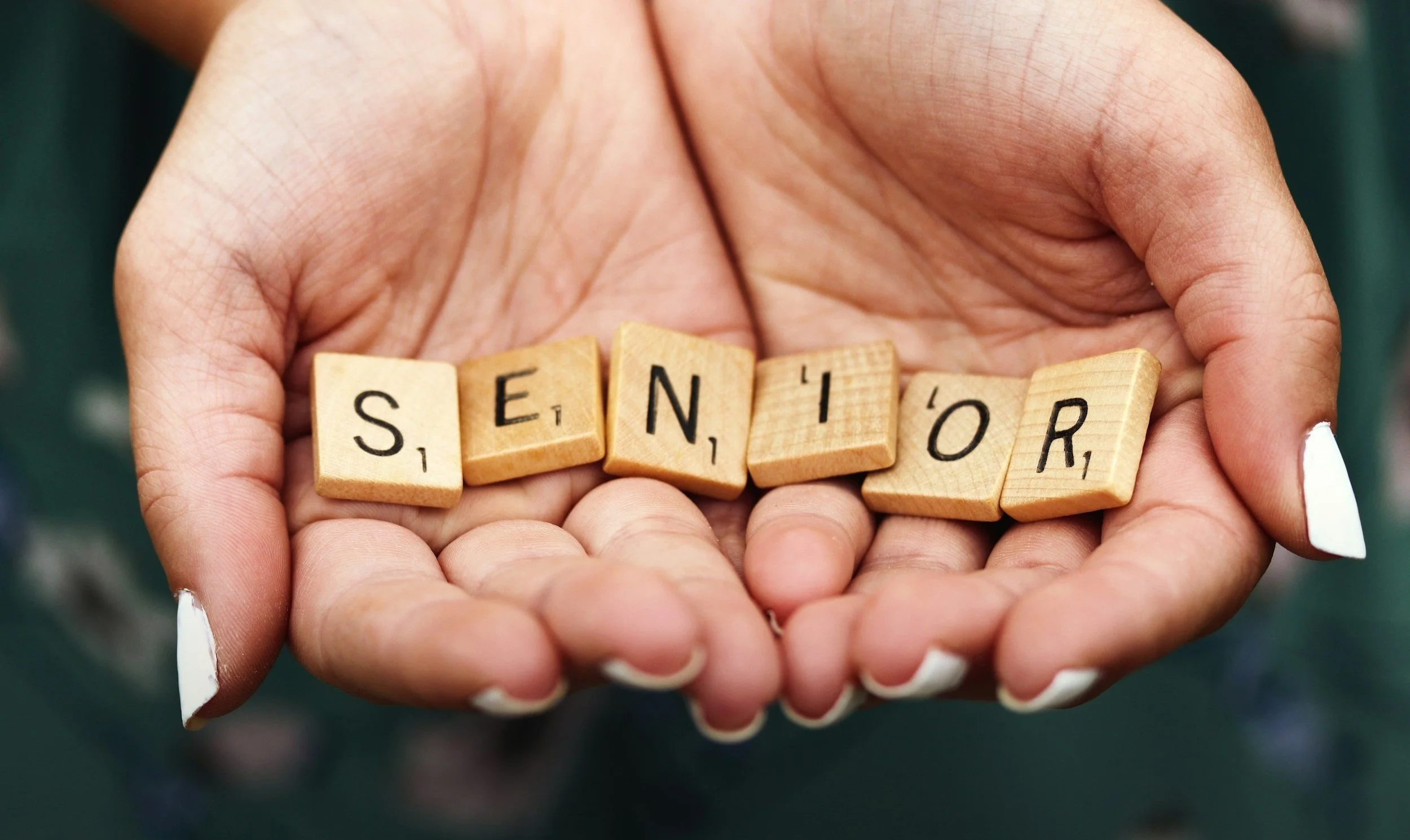 Une main tient des lettres en bois formant le mot "SENIOR".