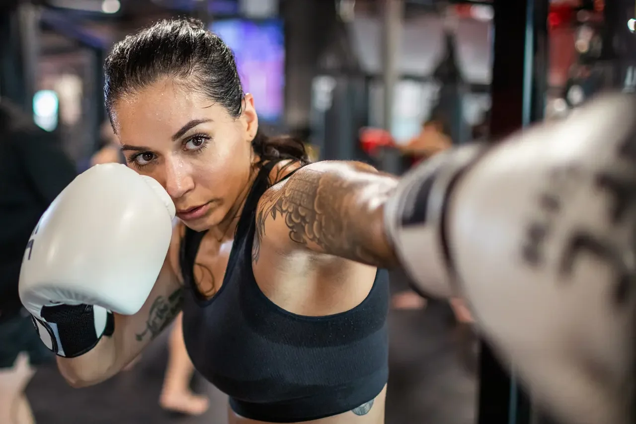 Woman wearing boxing gloves and athletic clothing punching in a gym.