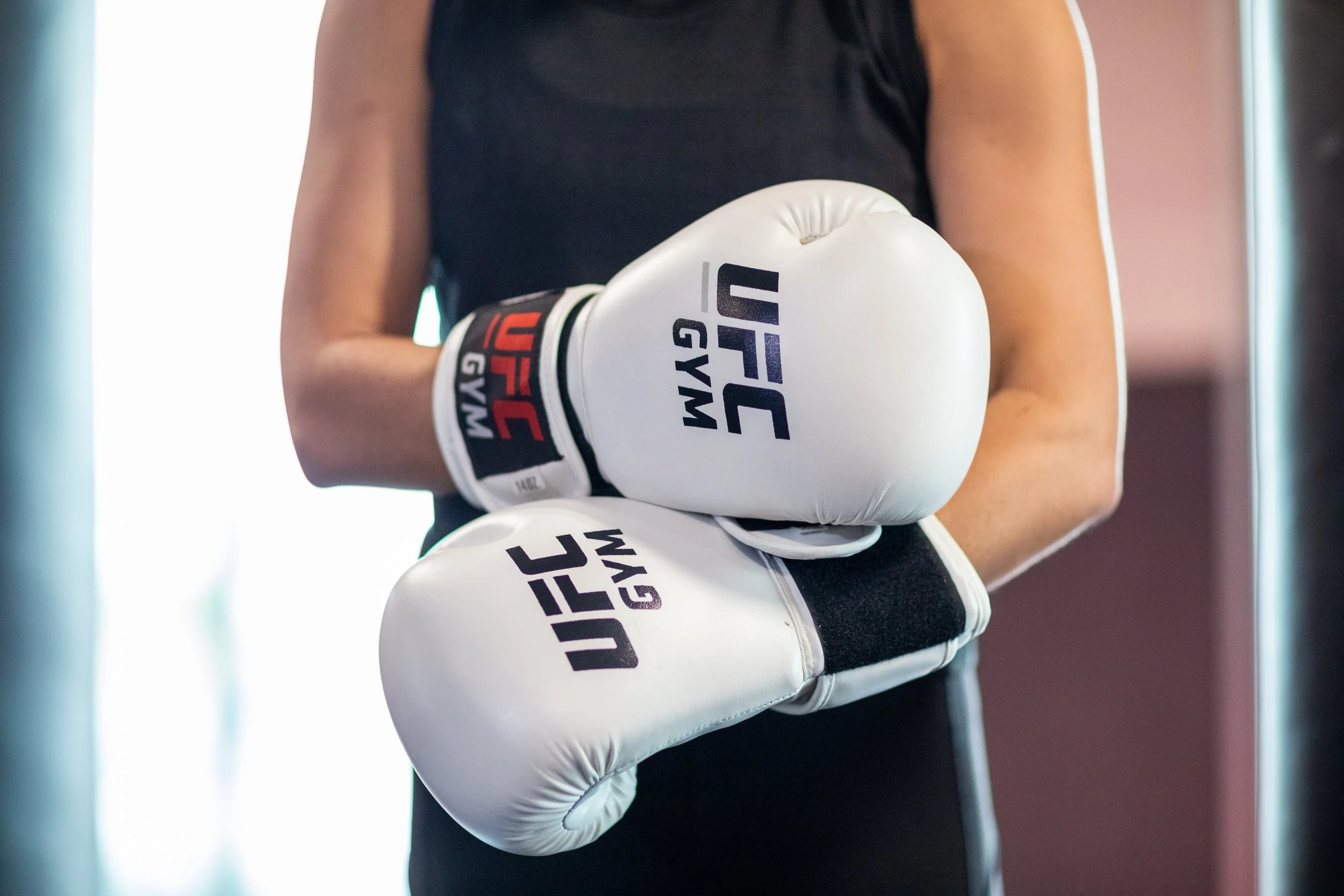 A person holding white boxing gloves with the words "USA GYM" printed on them, wearing a black sleeveless shirt.