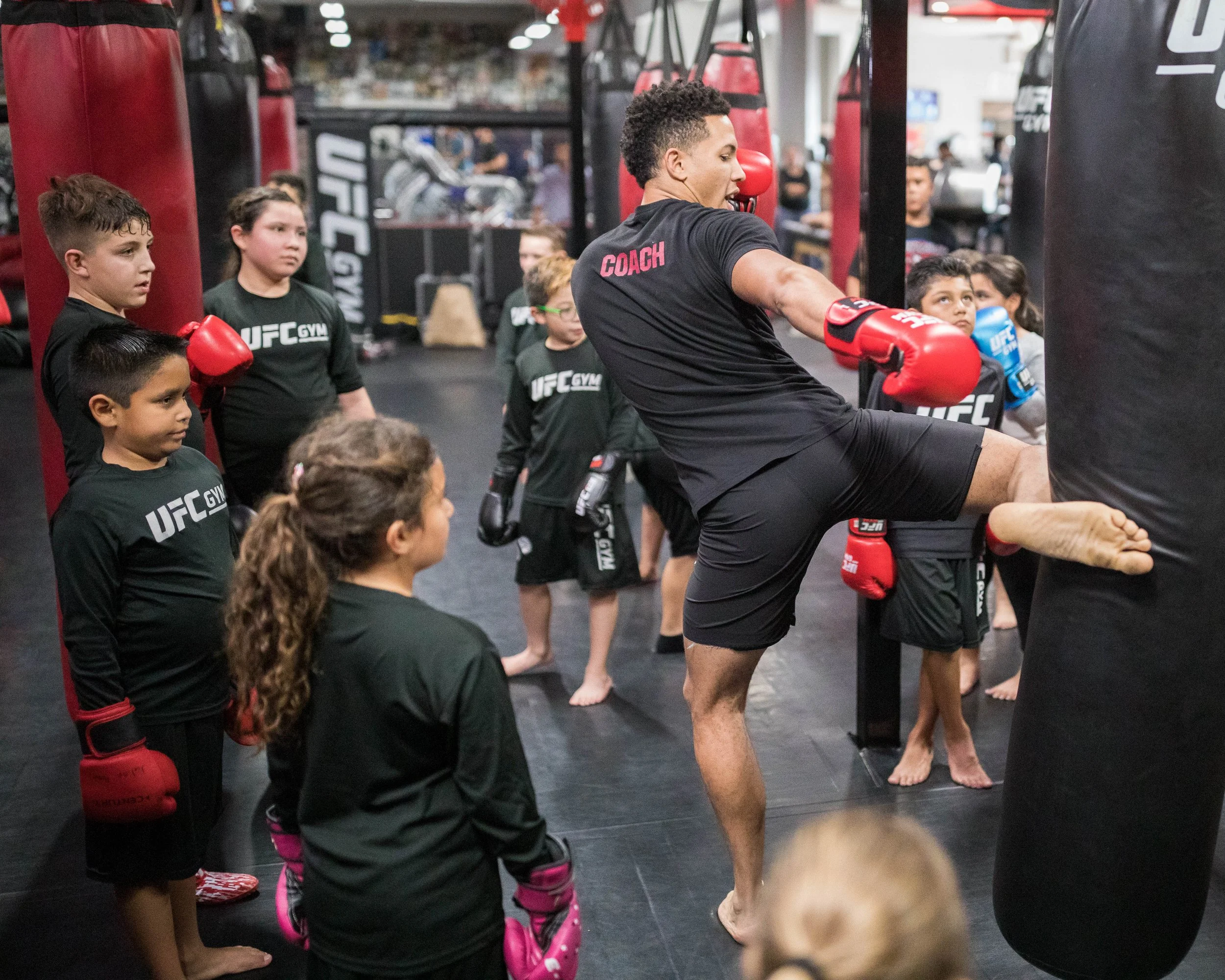 A group of children with boxing gloves listening to a coach in a gym.