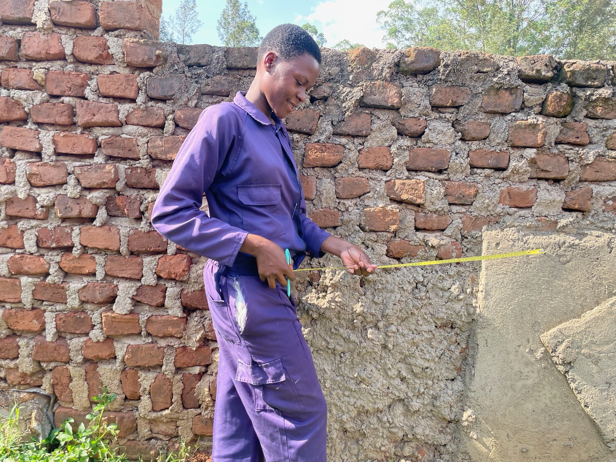 Esther, a bricklaying student at Bududa Vocational Academy, measuring a wall as part of her training.
