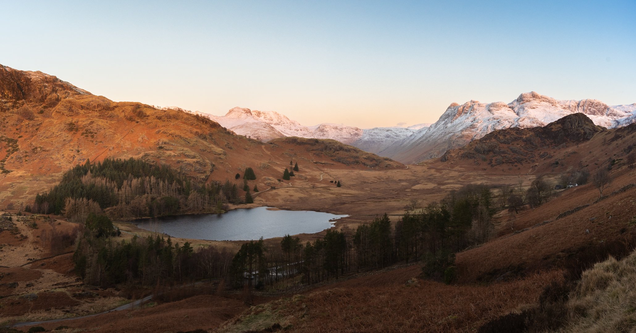 A scenic landscape with mountains, a lake, and rolling hills during sunset, Lake District.
