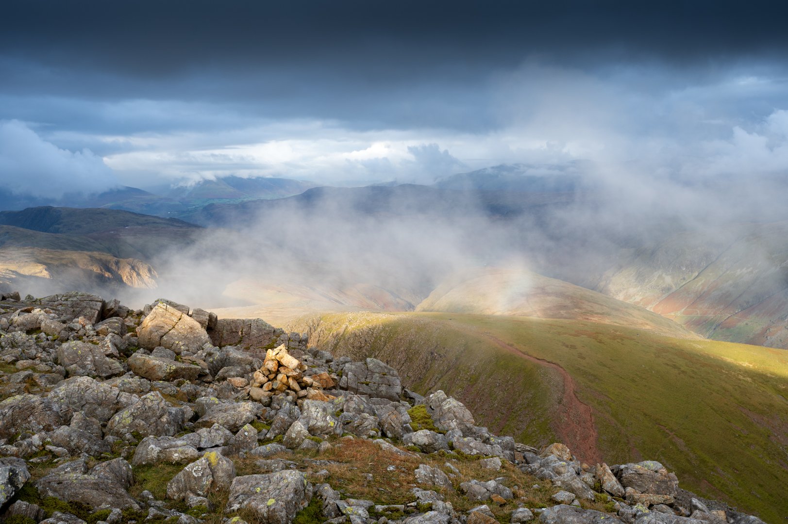 View of rugged mountains with rocky foreground, mist and clouds in the valleys, and dark clouds in the sky, Great Gable Lake District. 