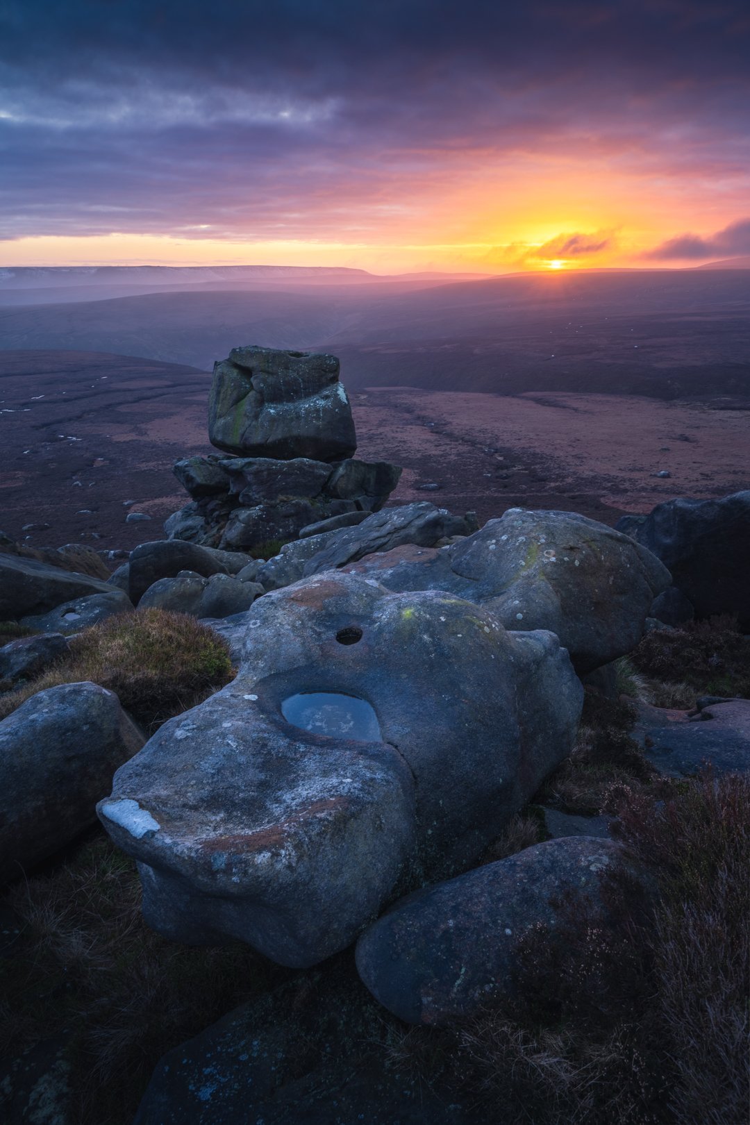 Sunset over a rocky landscape with large boulders and a cloudy sky.