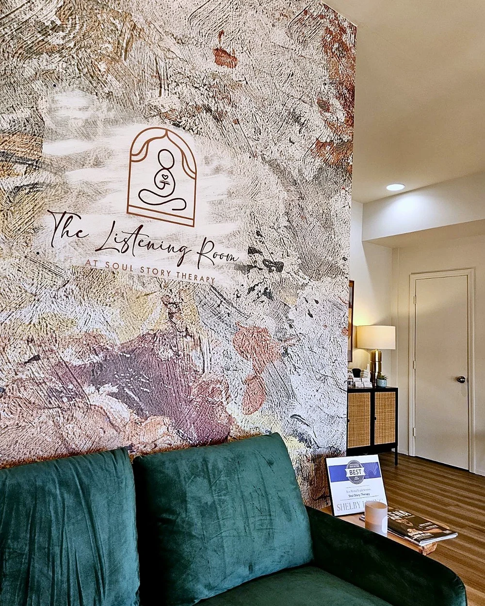 A green velvet couch beneath a hand-painted mural with The Listening Room at Soul Story Therapy logo in Helena