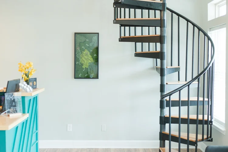 A bright front entry with a teal welcome desk, moss art, and a spiral staircase