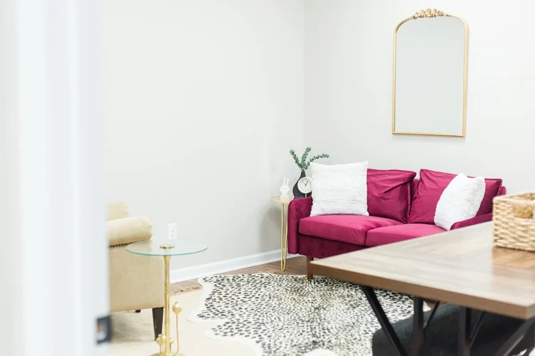 A therapy room with a pink velvet couch, gold mirror, and soft rug