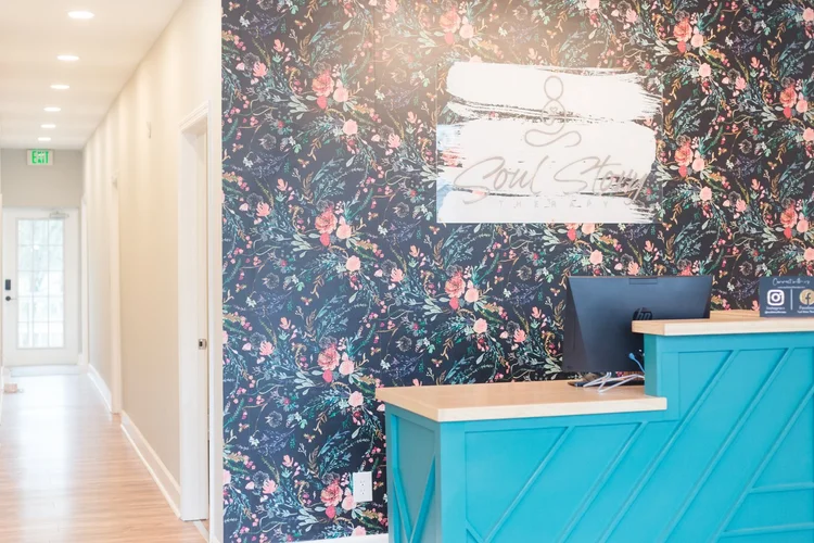 The front desk and hallway with a floral wallpaper wall and the Soul Story logo