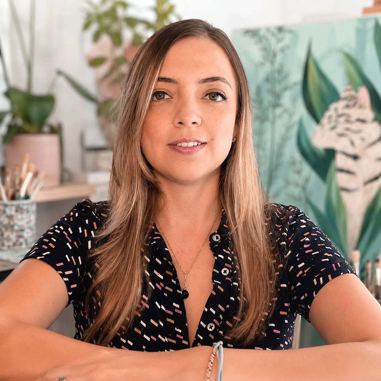 Sandra Mejia looking at the camera with one of her murals painted in the back wall