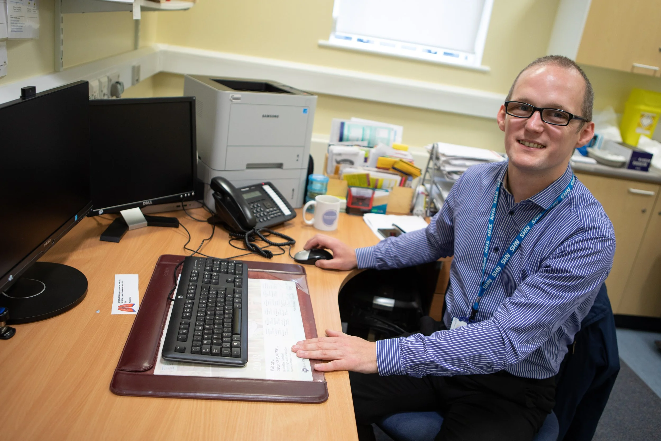 A man sat next to a desk with a computer and keyboard.