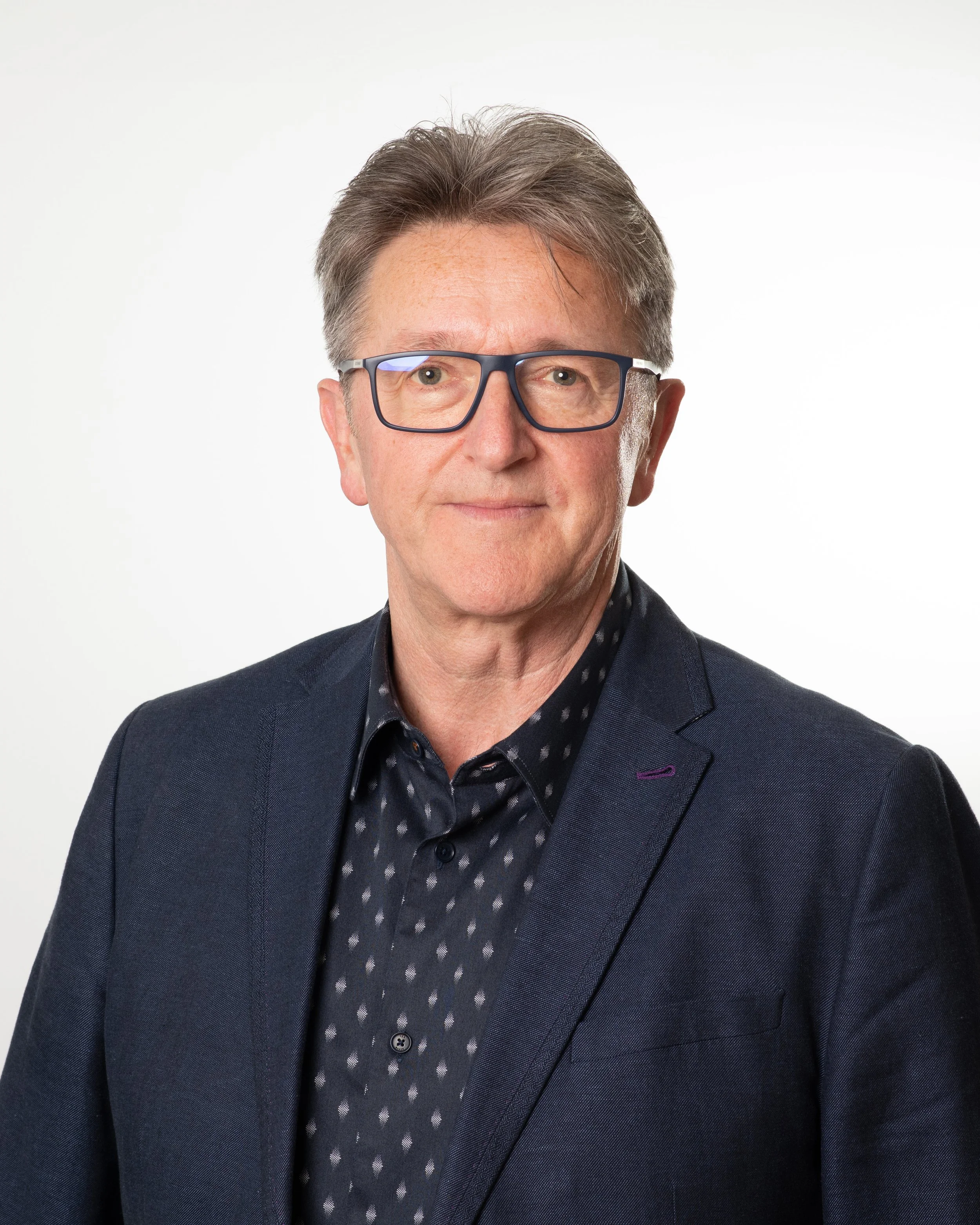 A middle aged man with a smart jacket, glasses and greying hair smiles to camera.