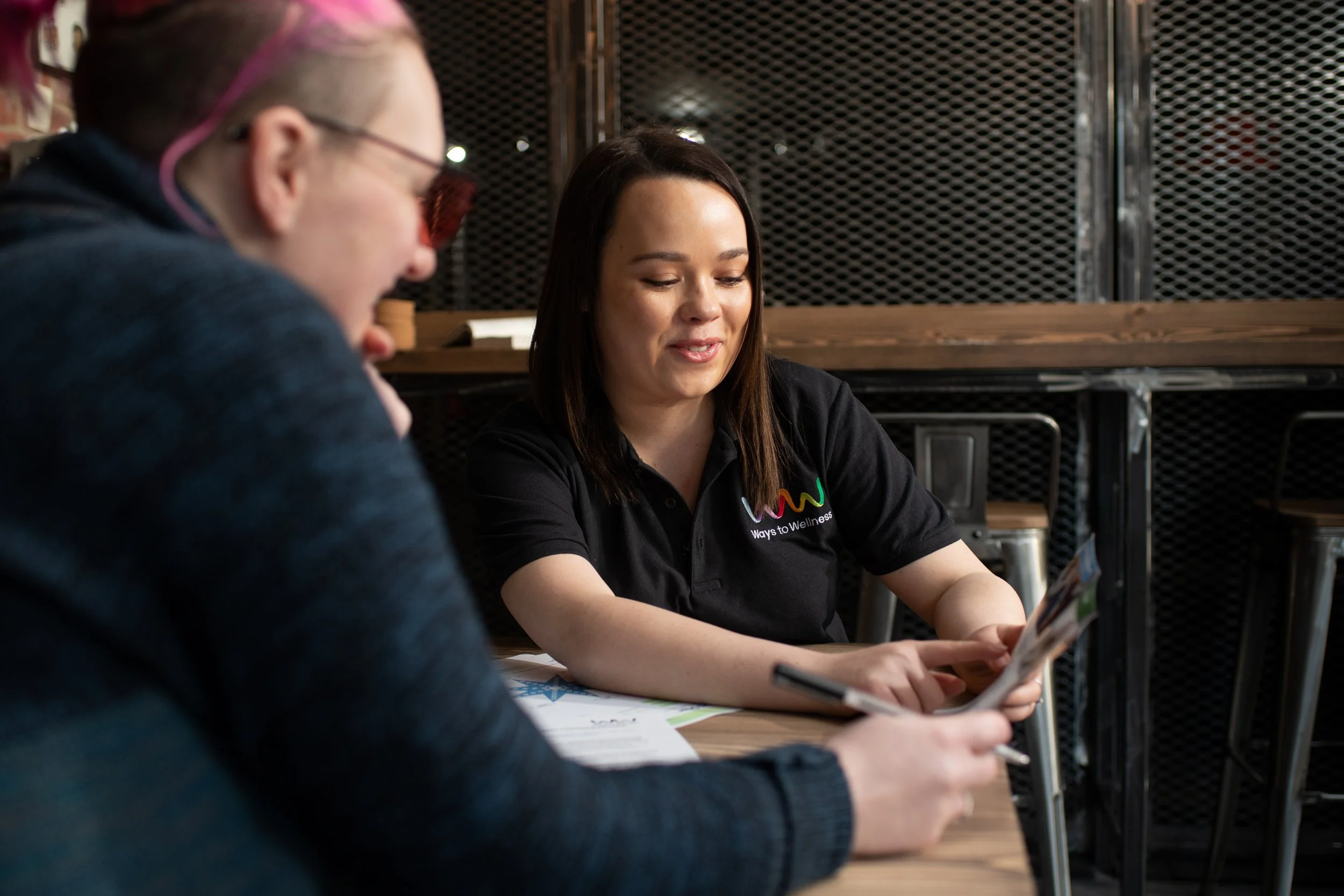 A woman holding a piece of paper for another woman to look at.