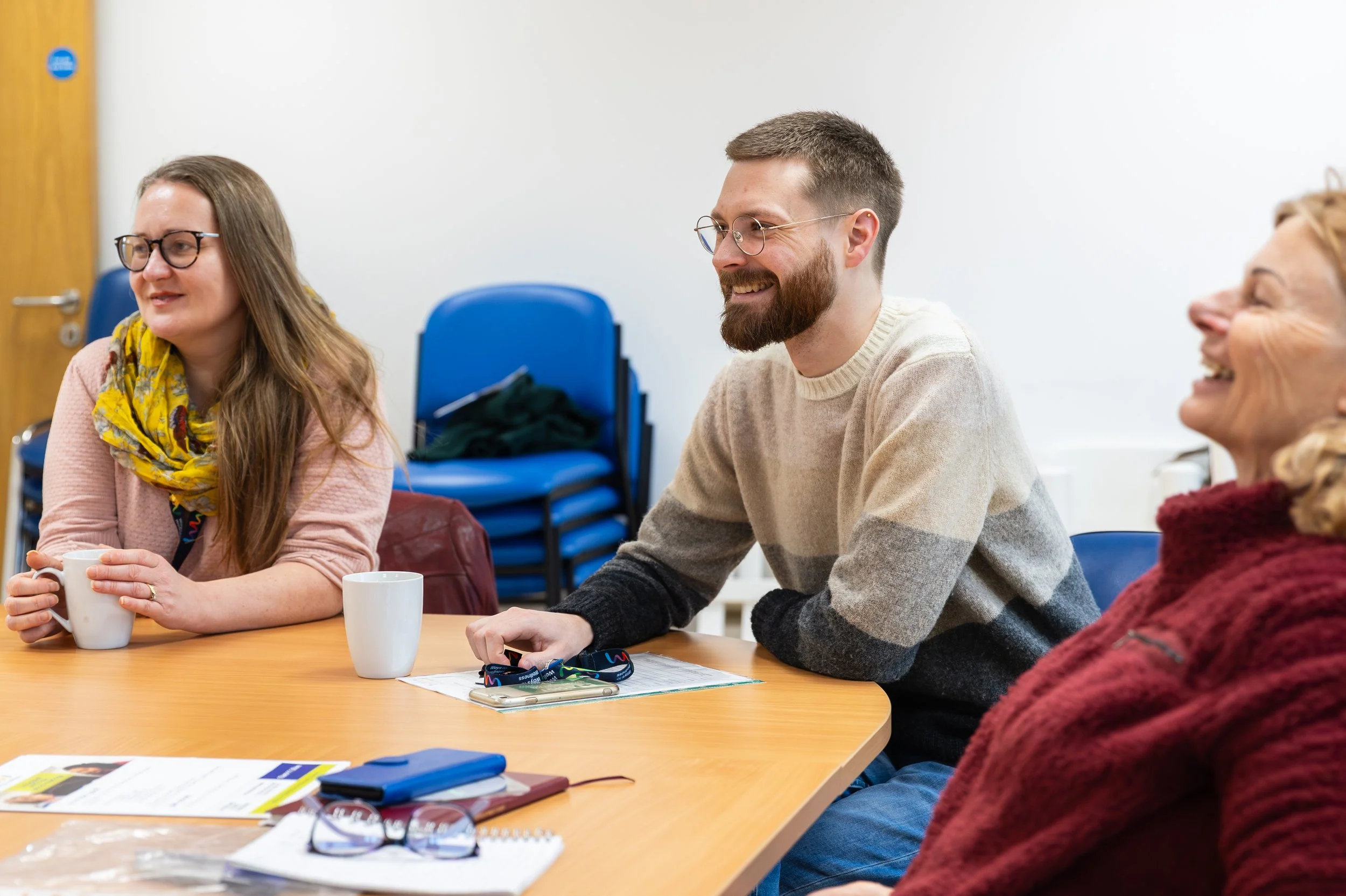 Three people who are smiling, sat around a table.
