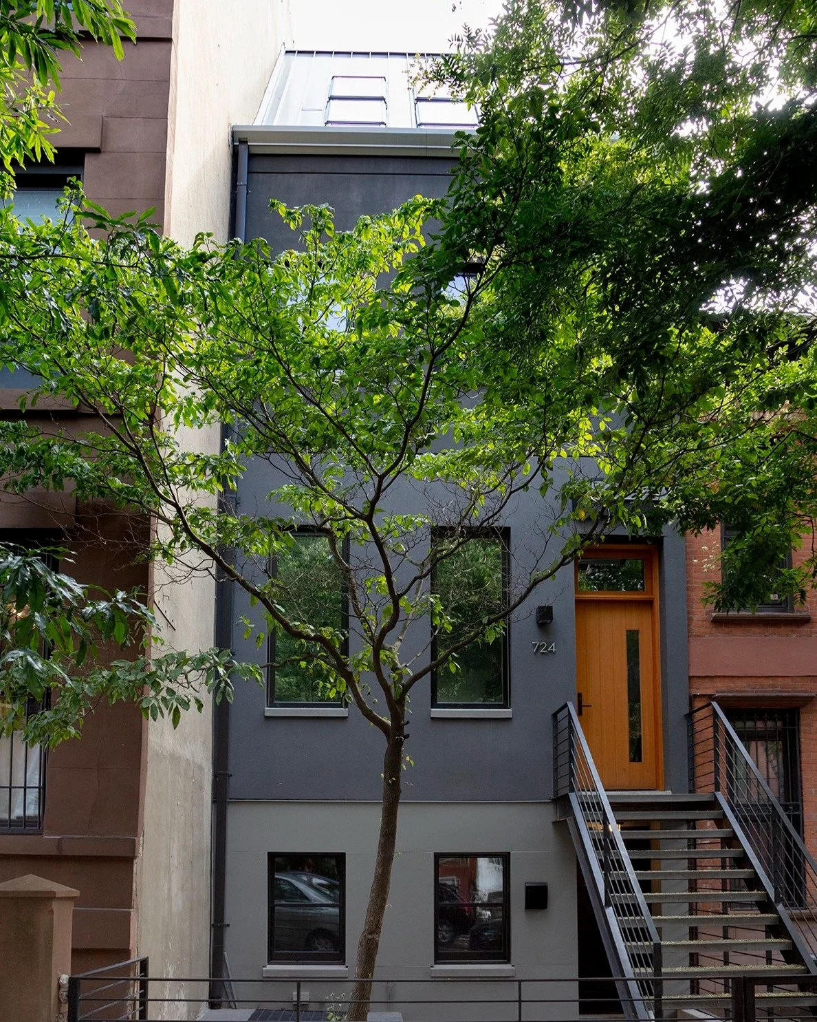 This full-floor rooftop addition sits at the treetop level, creating a dramatic double-height interior space with a perforated metal staircase connecting the levels, taking you to a rooftop terrace above. A grid of angled skylights forms a striking w