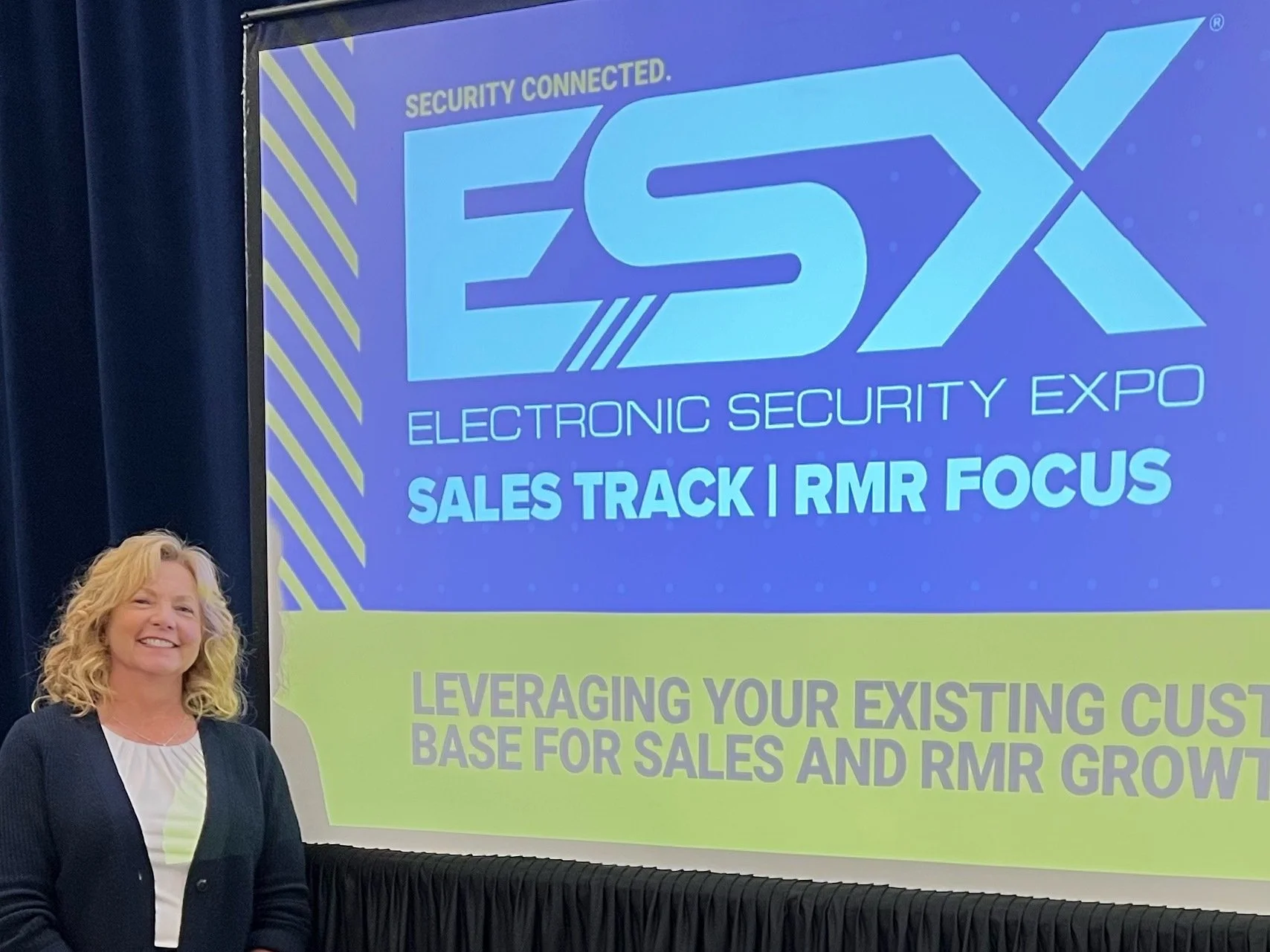 Person standing next to a presentation screen displaying "Electronic Security Expo, Sales Track | RMR Focus."