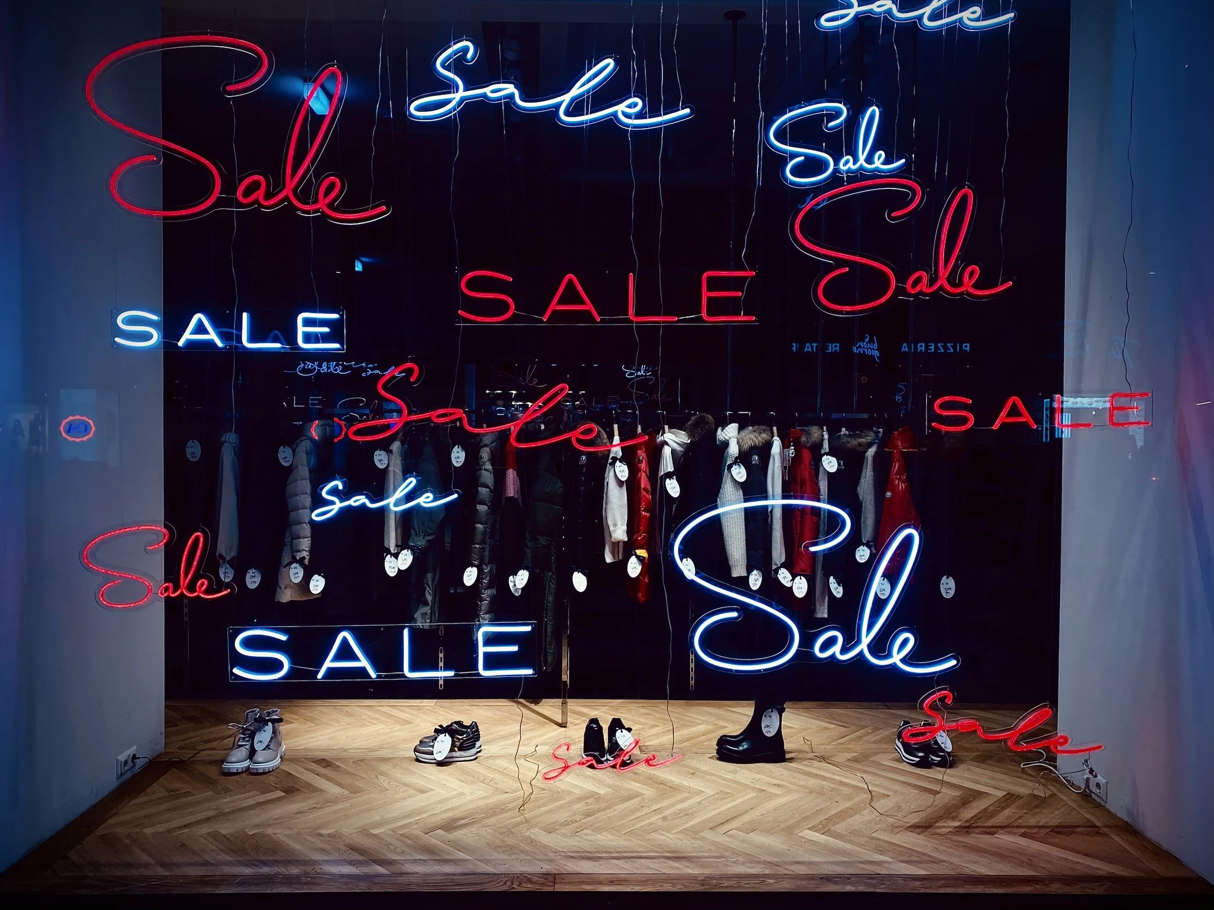 Store window display with "Sale" signs in neon lights and clothing items hanging on racks.