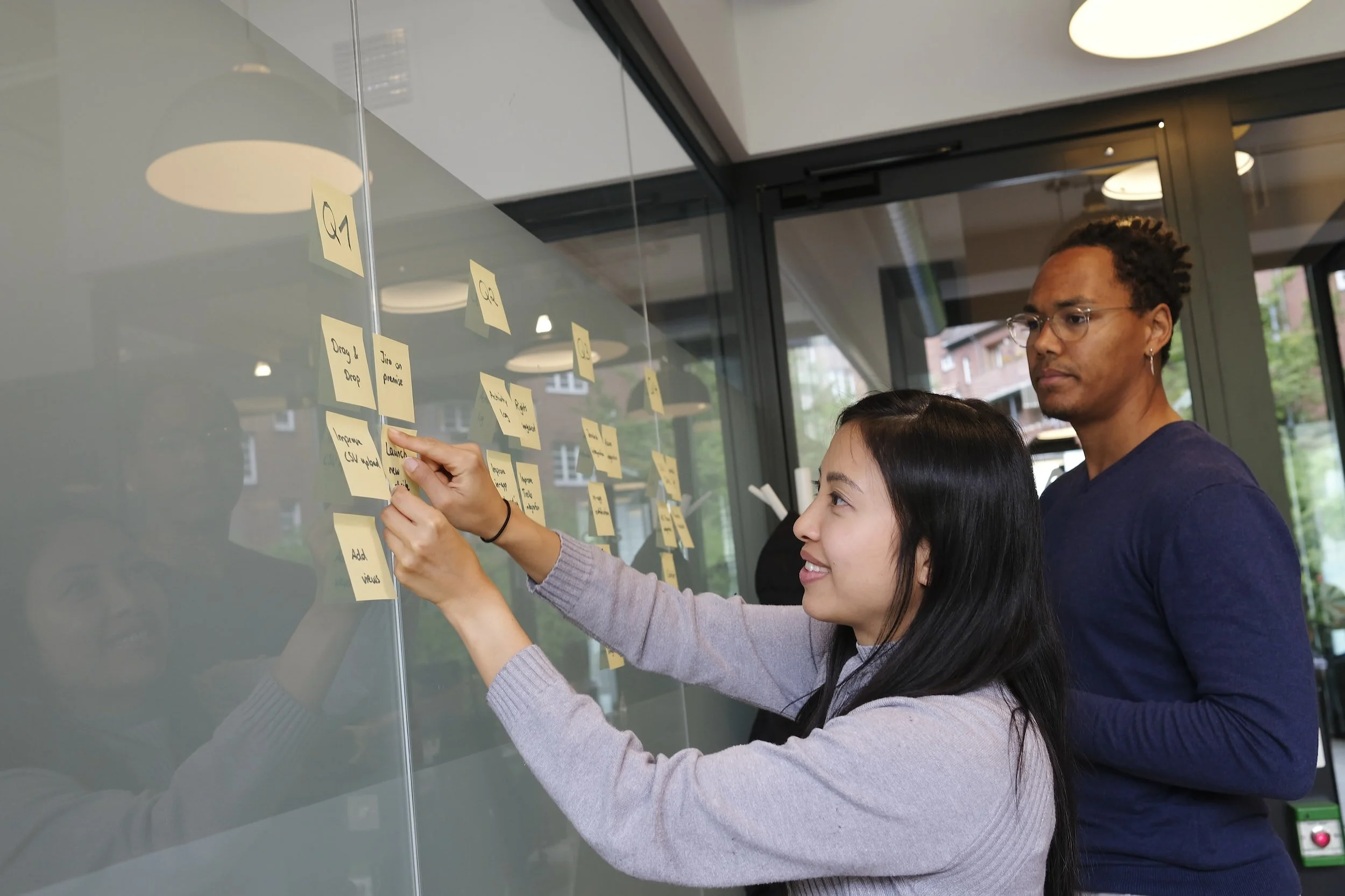 Two people brainstorming with sticky notes on a glass wall in an office environment.
