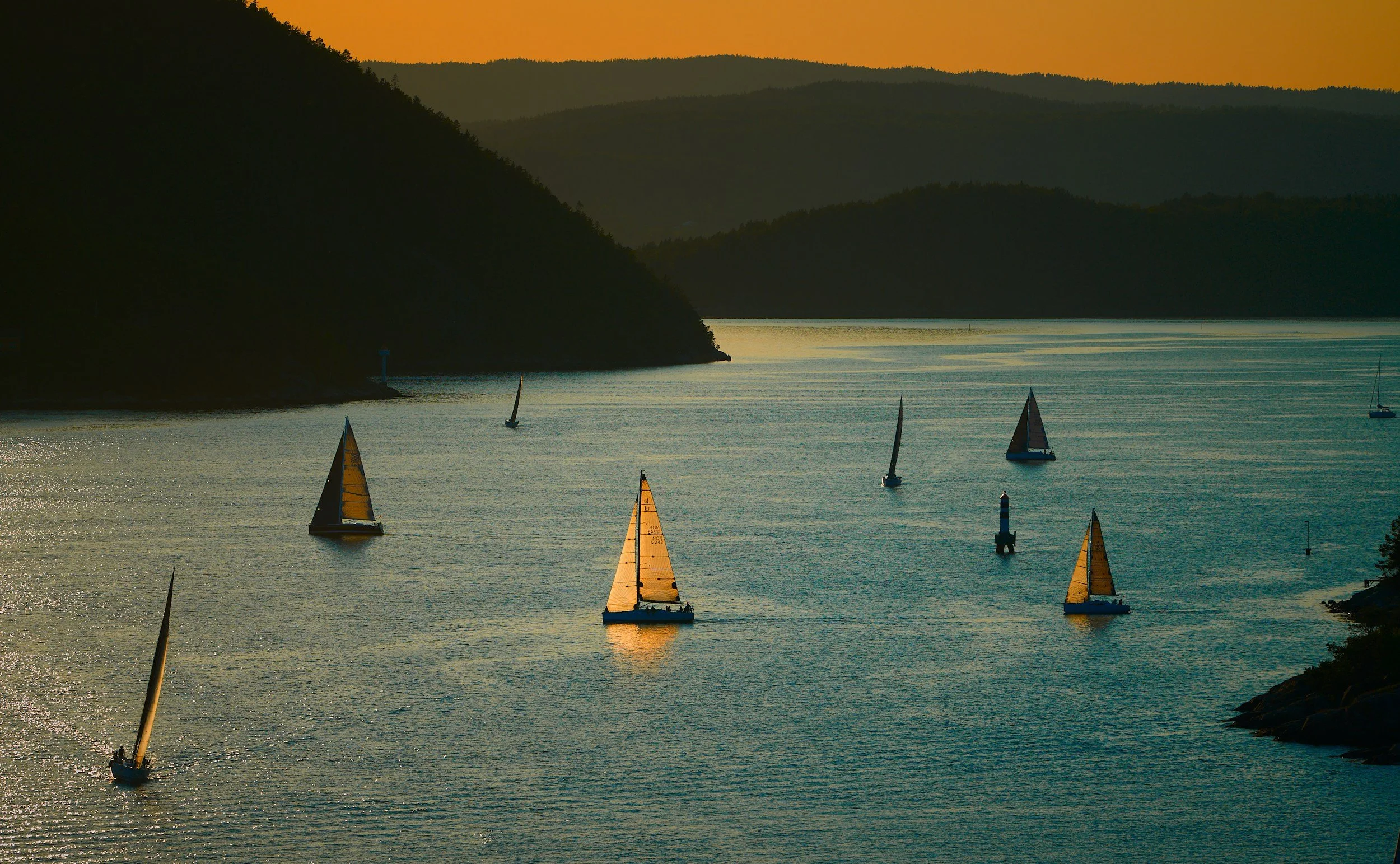 Sailboats on a calm body of water during sunset with hills in the background.