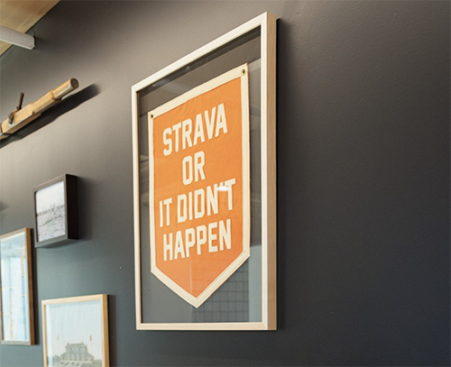 Framed sign on a dark gray wall with orange background and white text that reads 'STRAVA OR IT DIDN'T HAPPEN'.