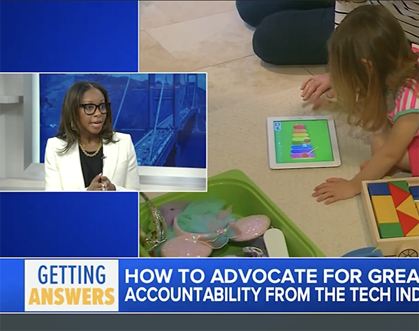 A television screen shows a news program with a woman speaking, and a young girl is playing with a tablet and educational toys on the floor.