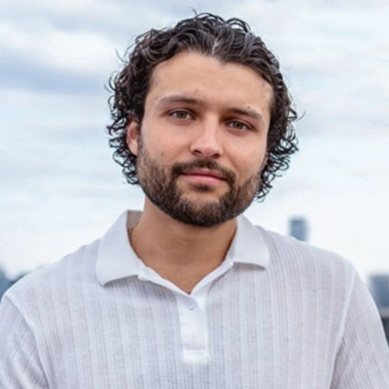 Person with curly hair and beard wearing a white shirt outdoors