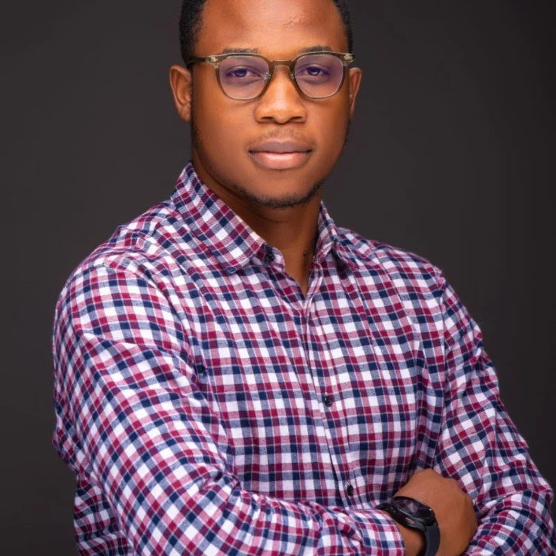Man wearing glasses and a checkered shirt with folded arms against a dark background.