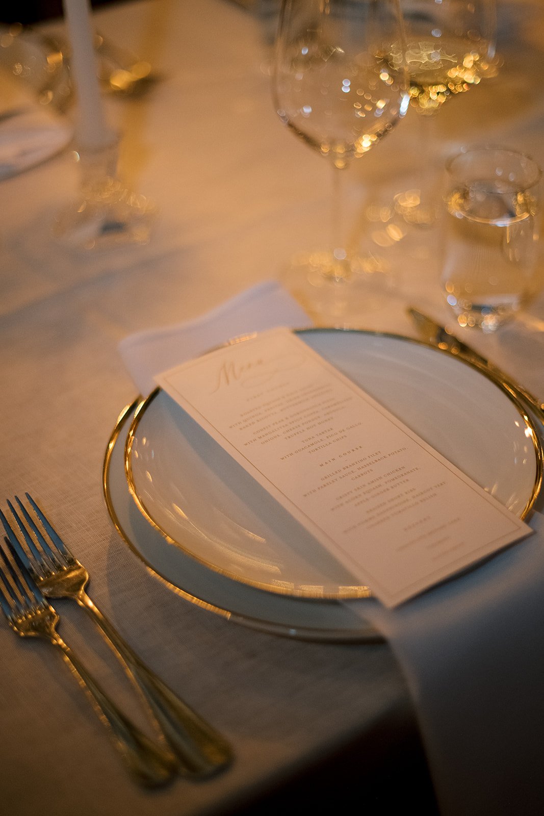 Elegant table setting with a plate, menu, cutlery, wine glass, and candle.