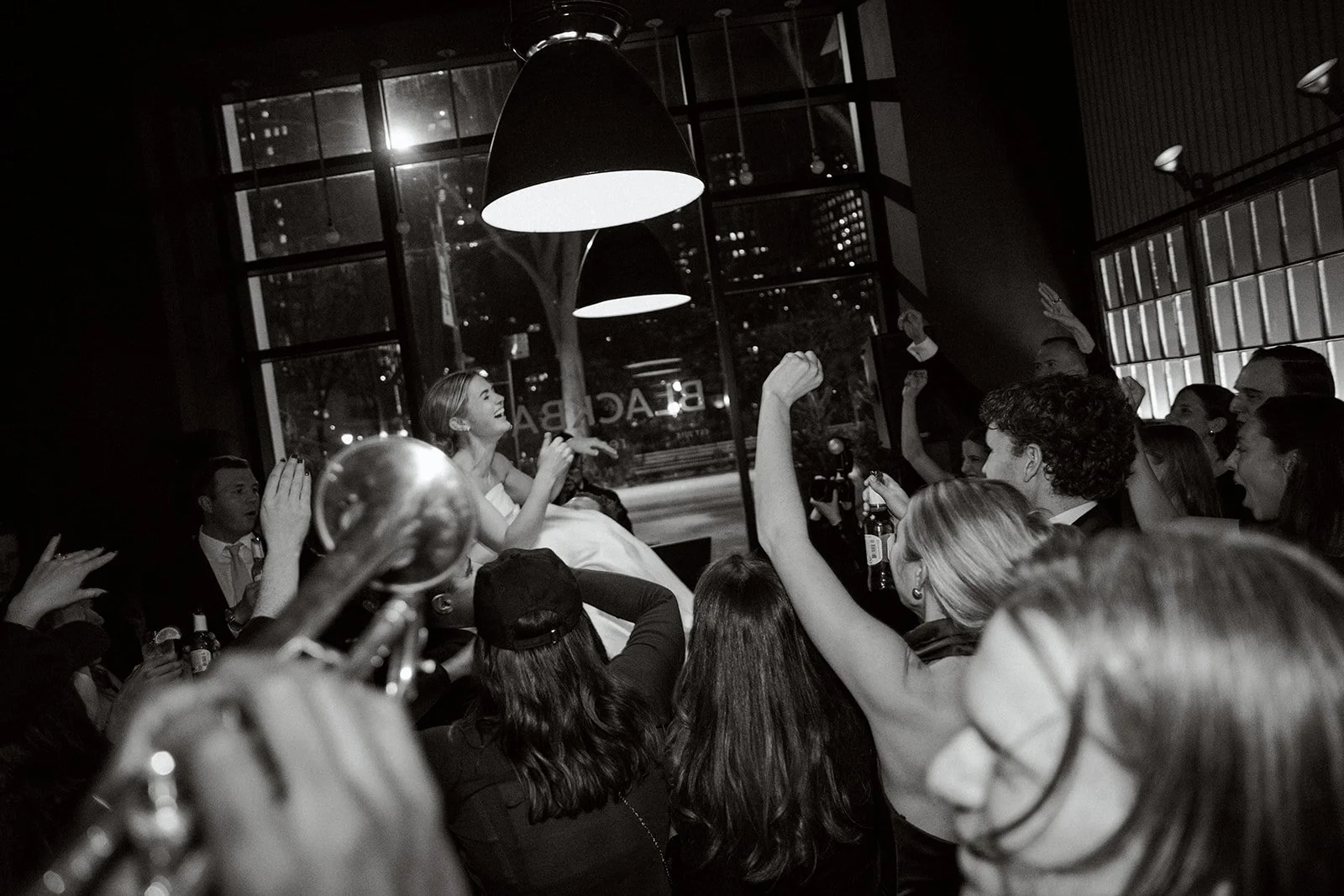 Wedding celebration with bride lifted in a crowded, festive room.