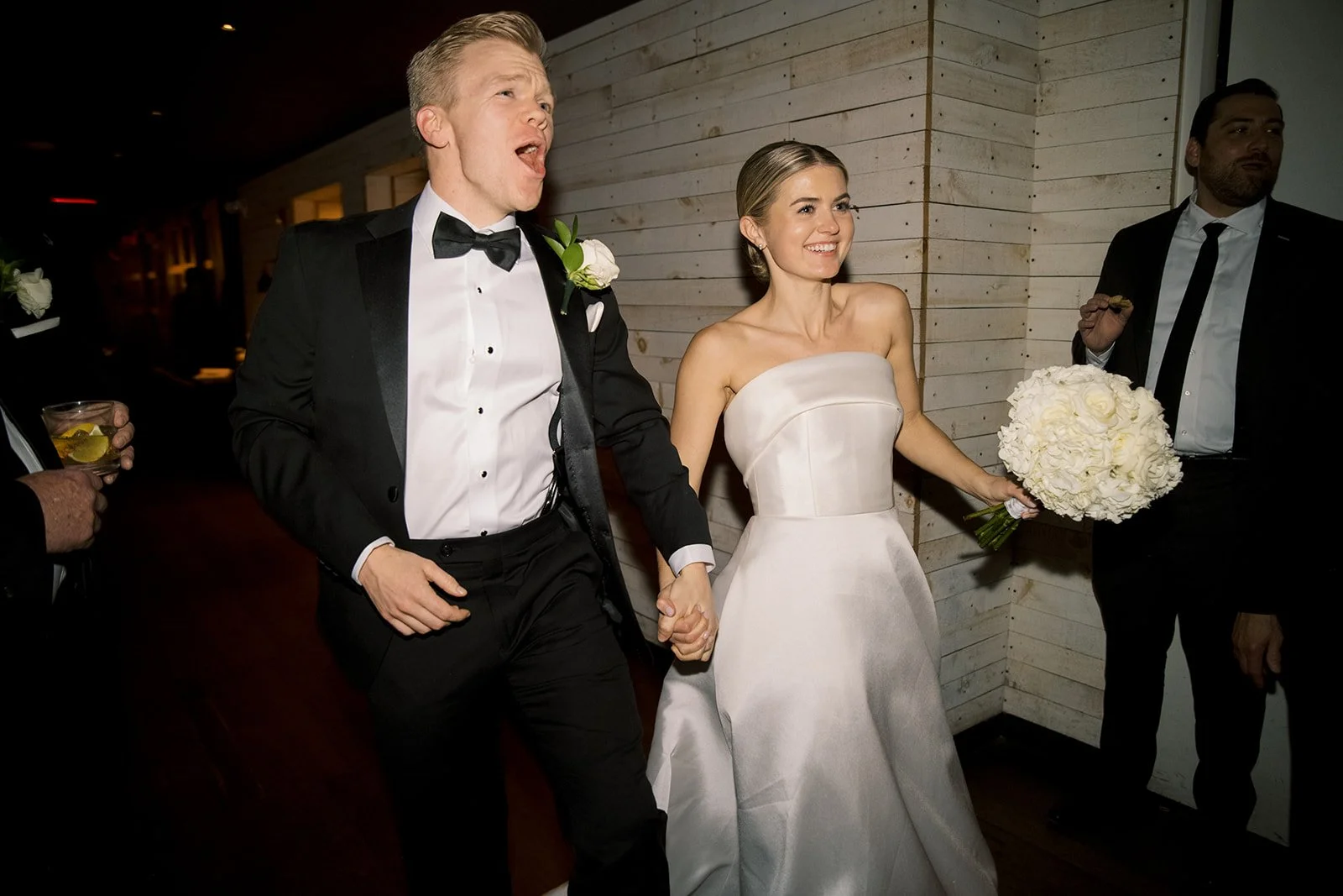 Bride and groom holding hands, bride holding a bouquet, in a wedding setting.