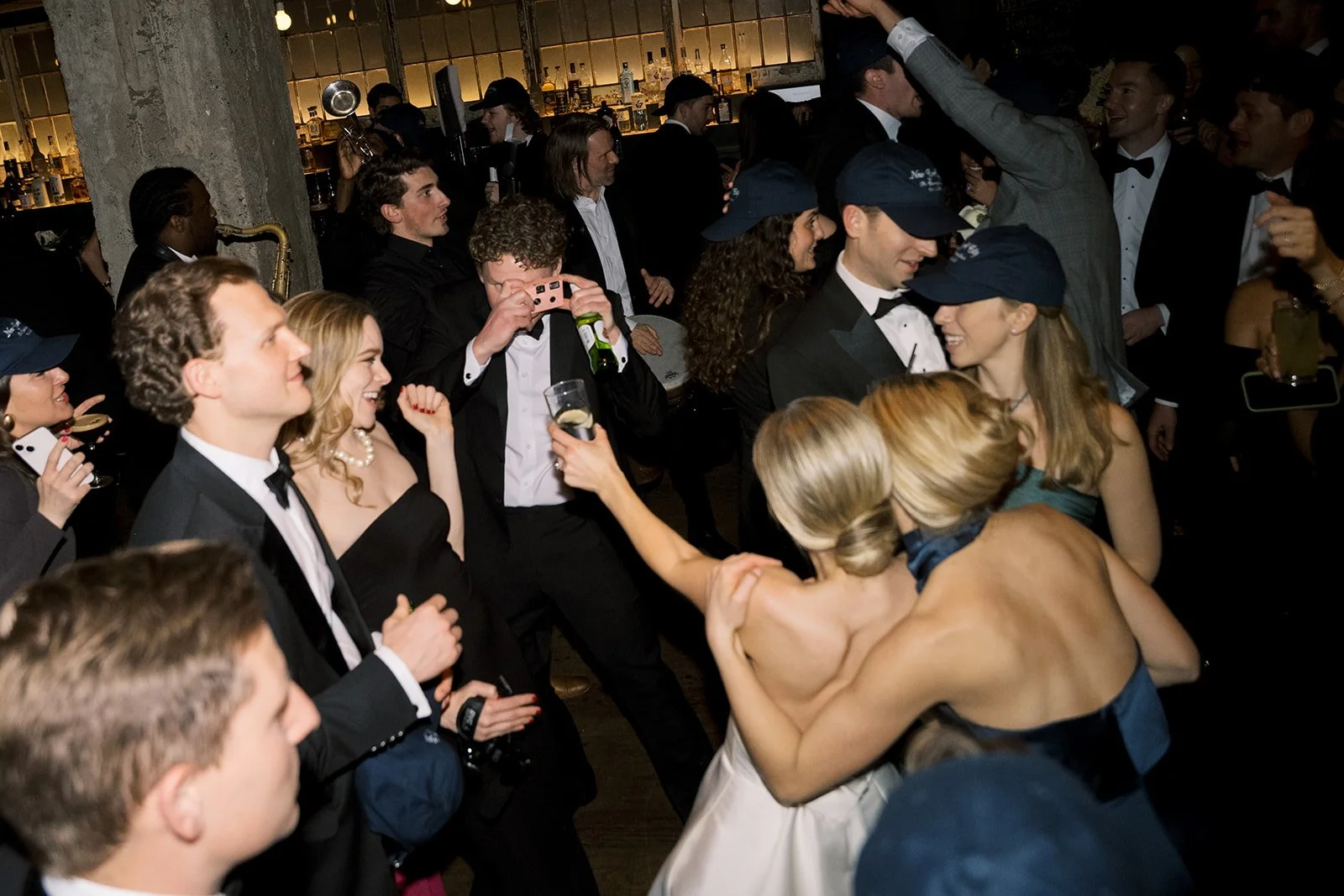 Group of people in formal attire dancing and celebrating at an indoor party with a live band.