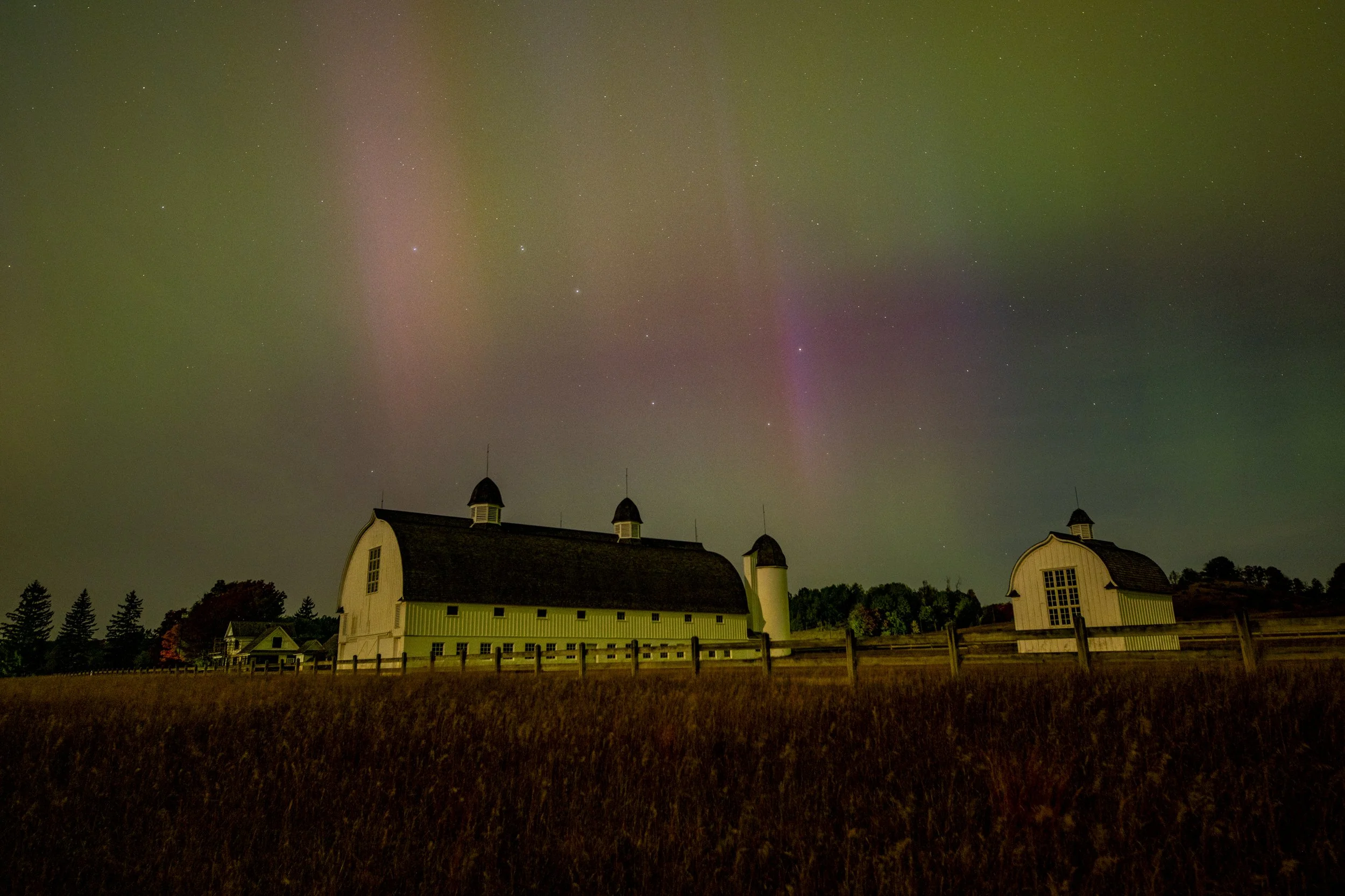 Barns under Northern Lights with a starry sky and grassy field.
