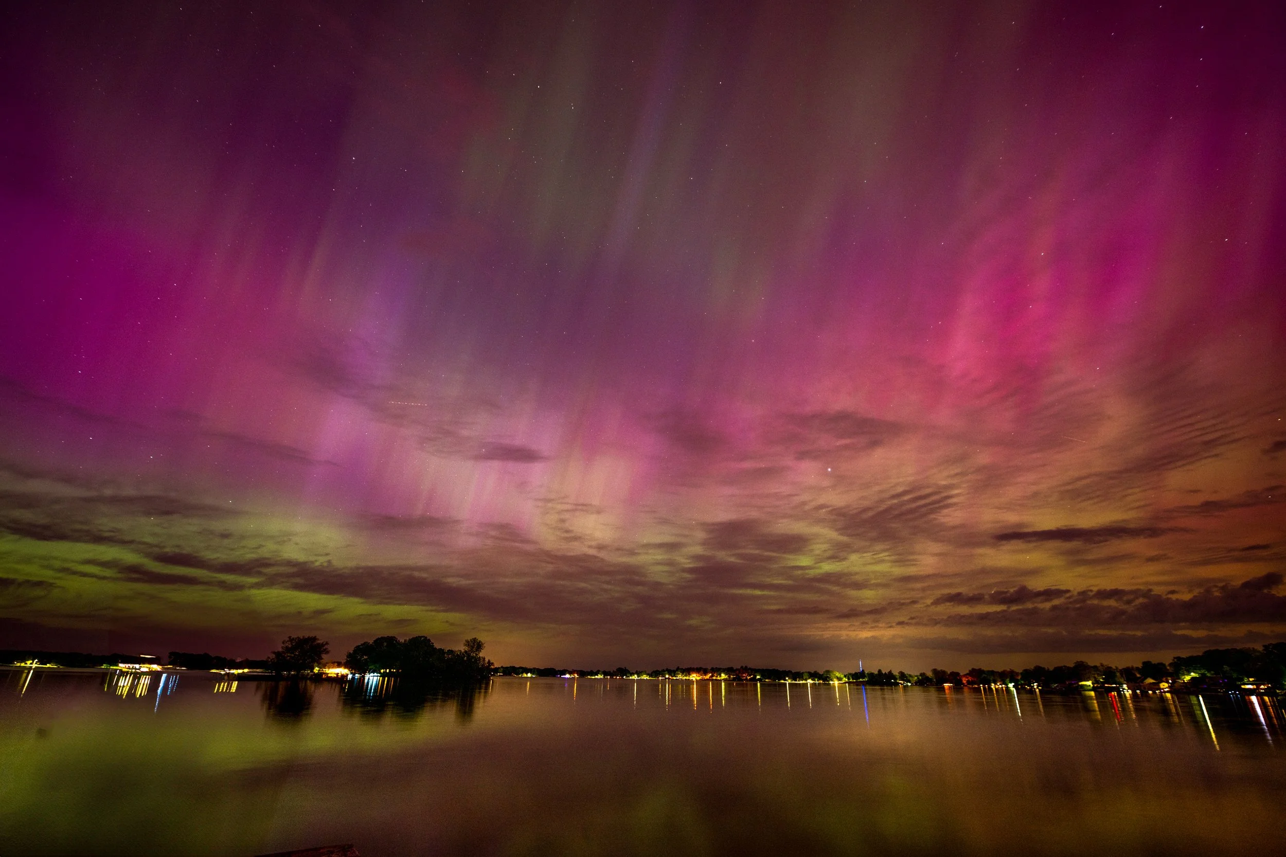 Vibrant Northern Lights reflecting on a calm lake with a dark horizon and colorful sky.