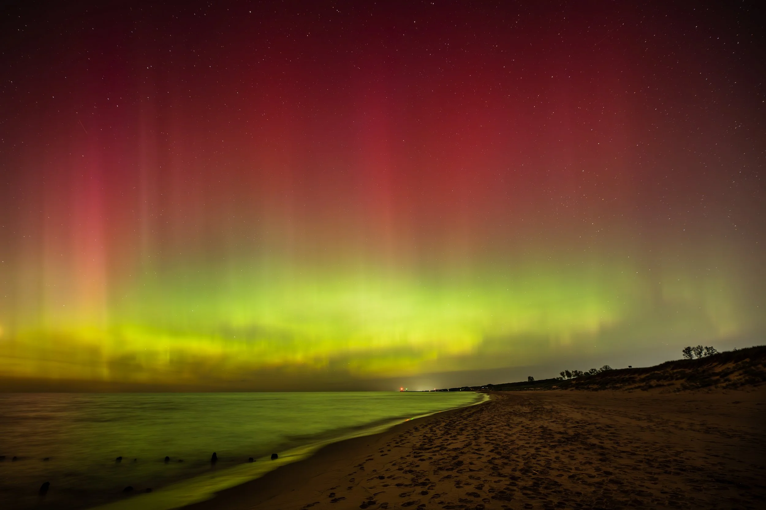 Aurora borealis with green and red lights over a calm beach at night.