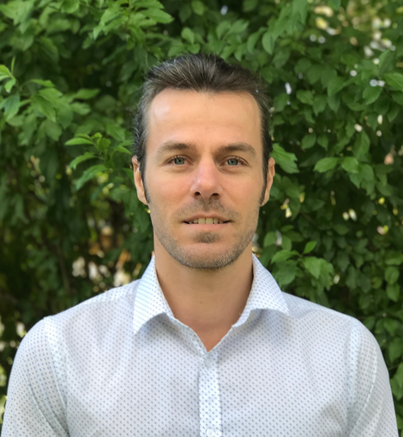 Man in white shirt standing in front of green leafy background