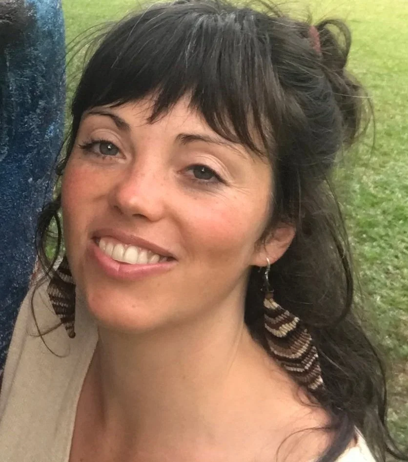 Woman with long dark hair and feather earrings, smiling outdoors
