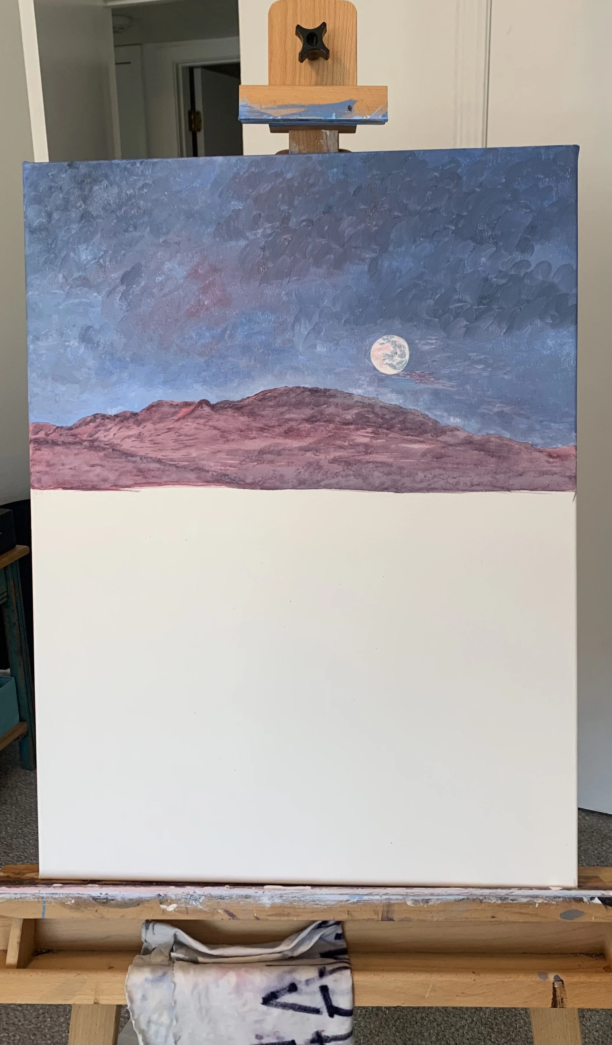 Canvas on easel with moonlit mountain landscape, unfinished painting.