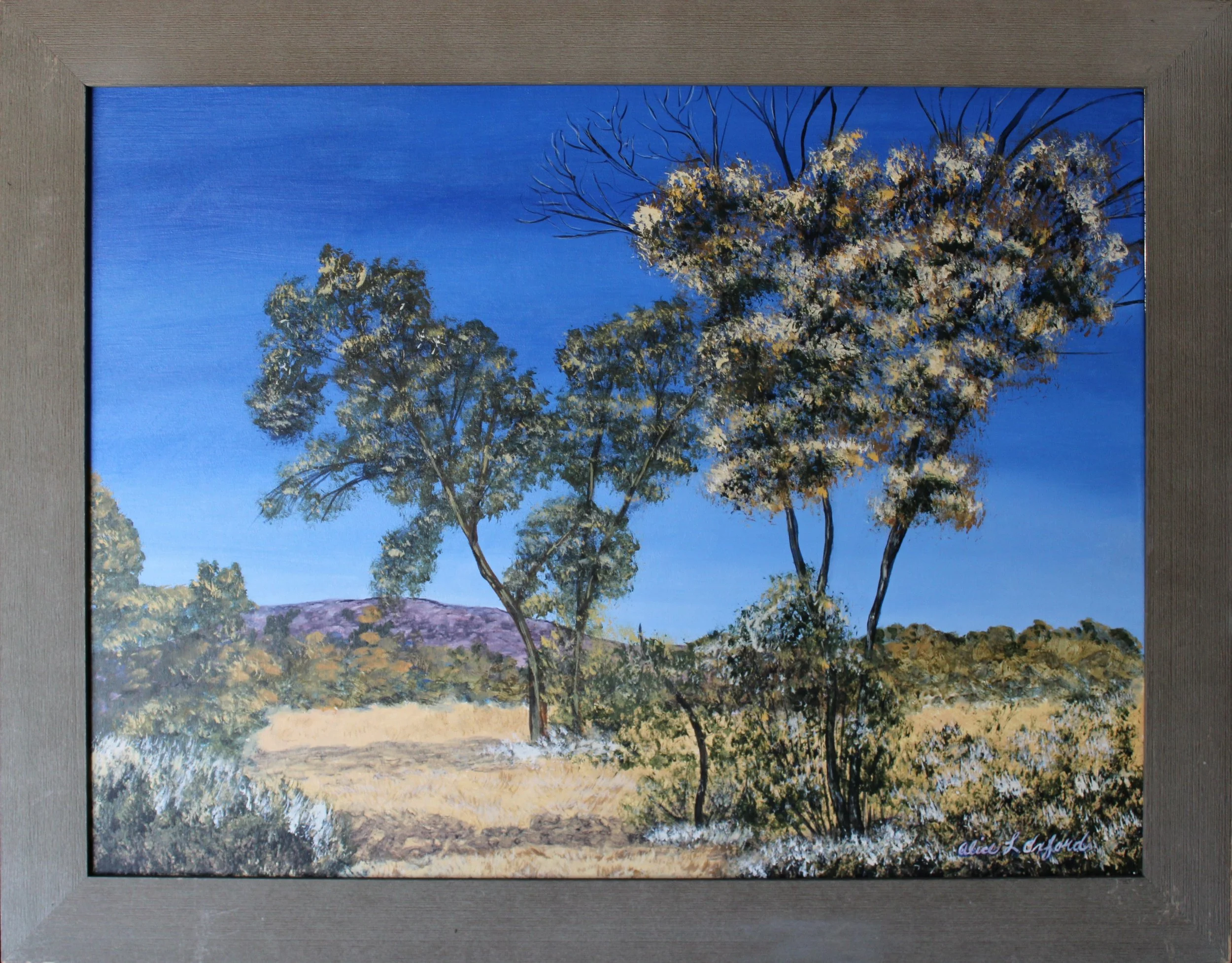 Alice Oxford's process photo of landscape painting with trees and blue sky in a gray wooden frame.