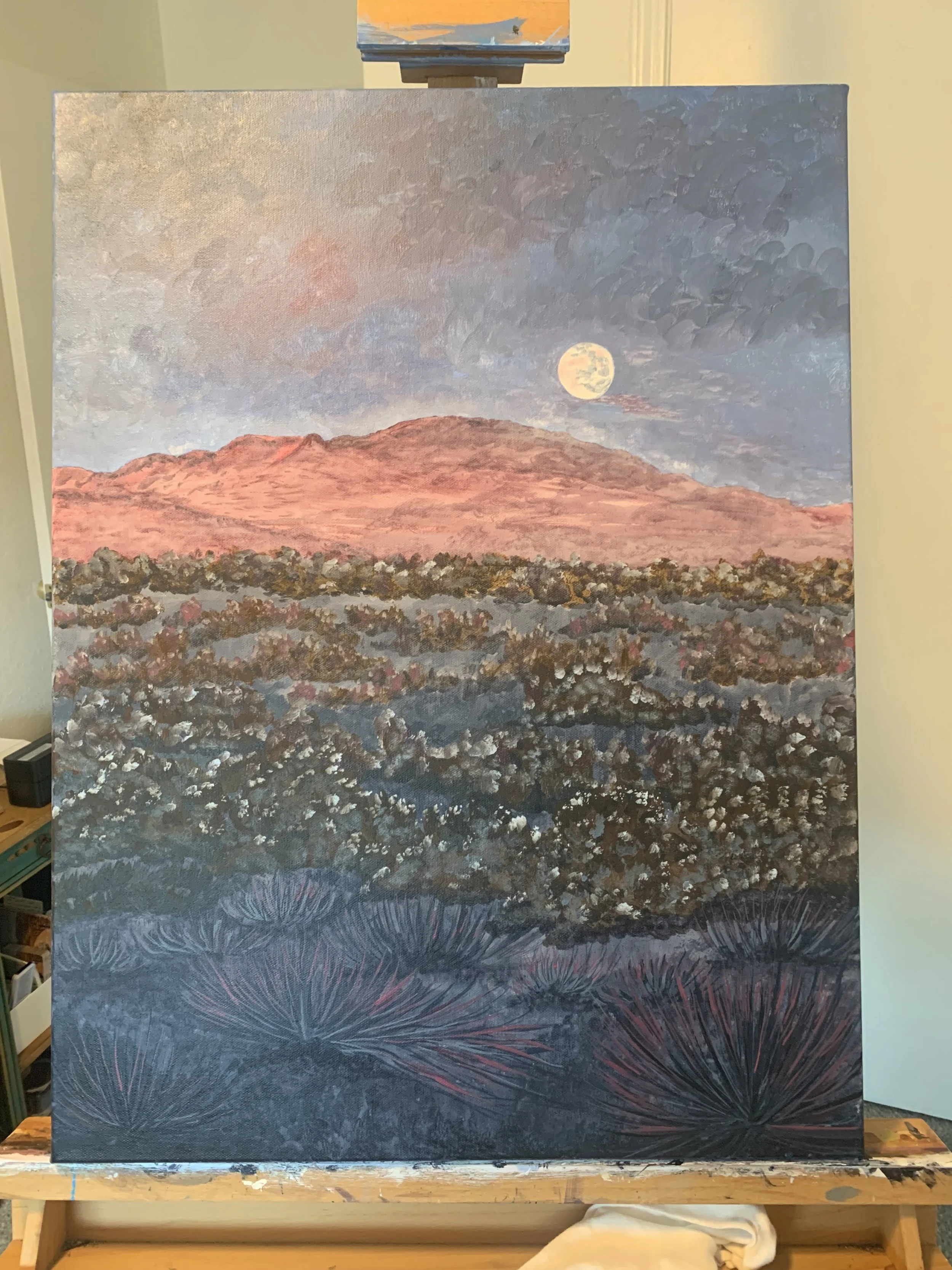 Painting of a desert landscape with a mountain range under a moonlit sky. The foreground features bushes and desert vegetation.