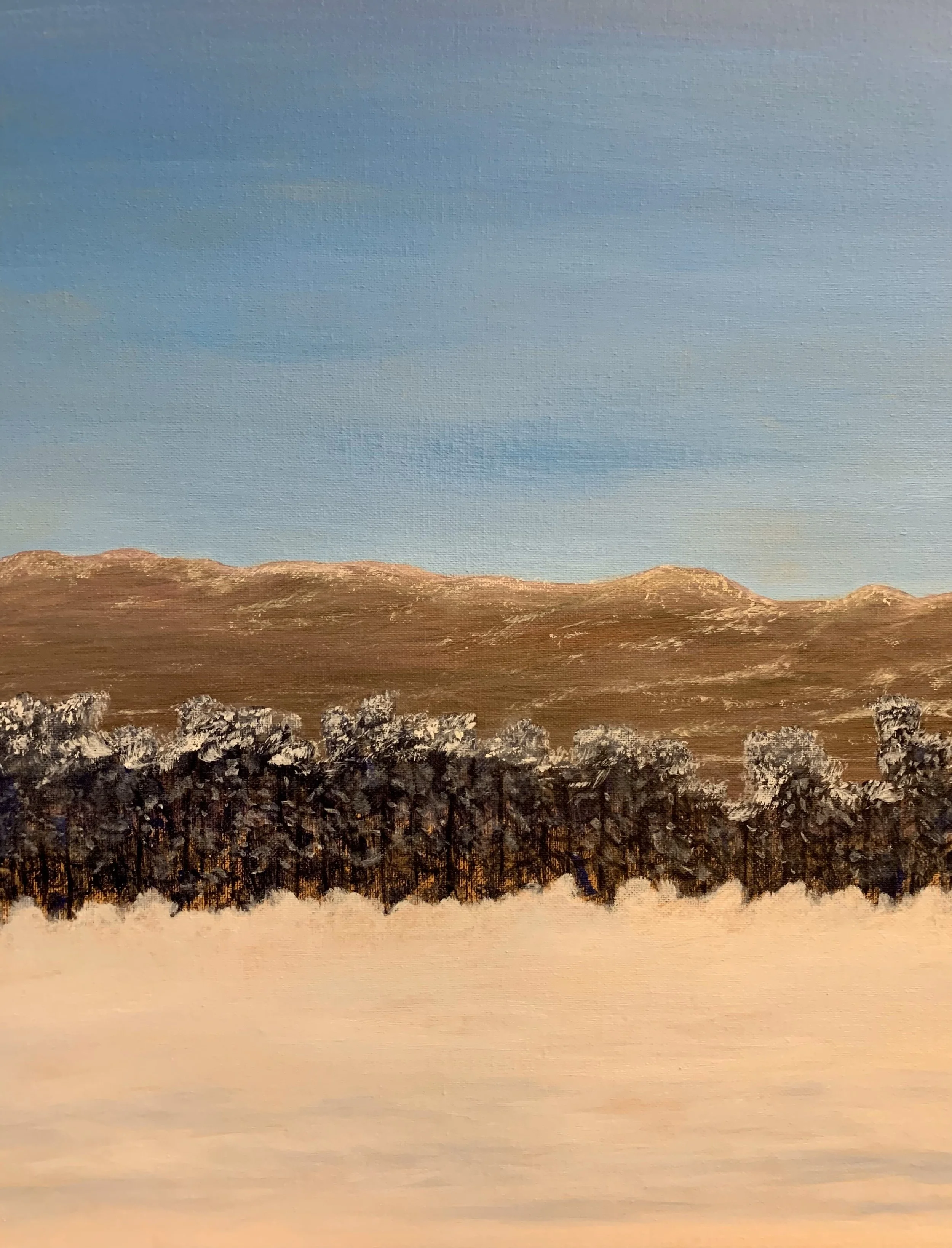 Alice Oxfords process photo of landscape painting depicting a winter scene with snowy ground, a row of leafless trees in the middle, and brown mountains in the background under a clear blue sky.