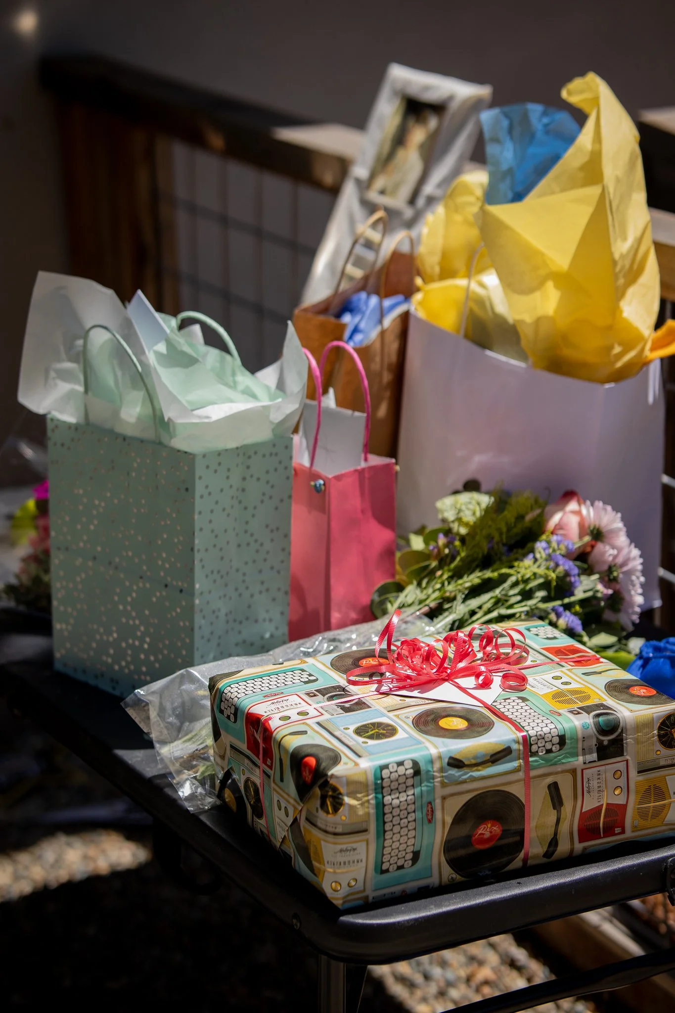 Gift table with colorful bags, floral wrapping paper, and a bouquet of flowers.