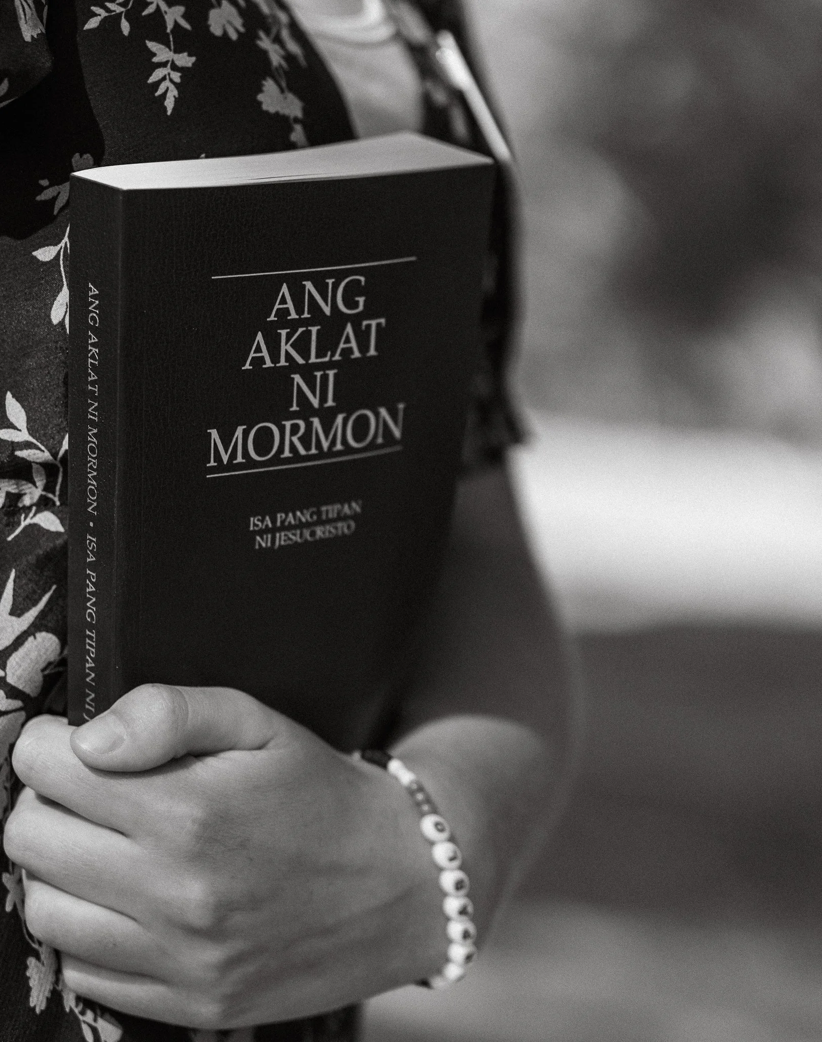 Person holding a book titled "Ang Aklat Ni Mormon," in black and white.
