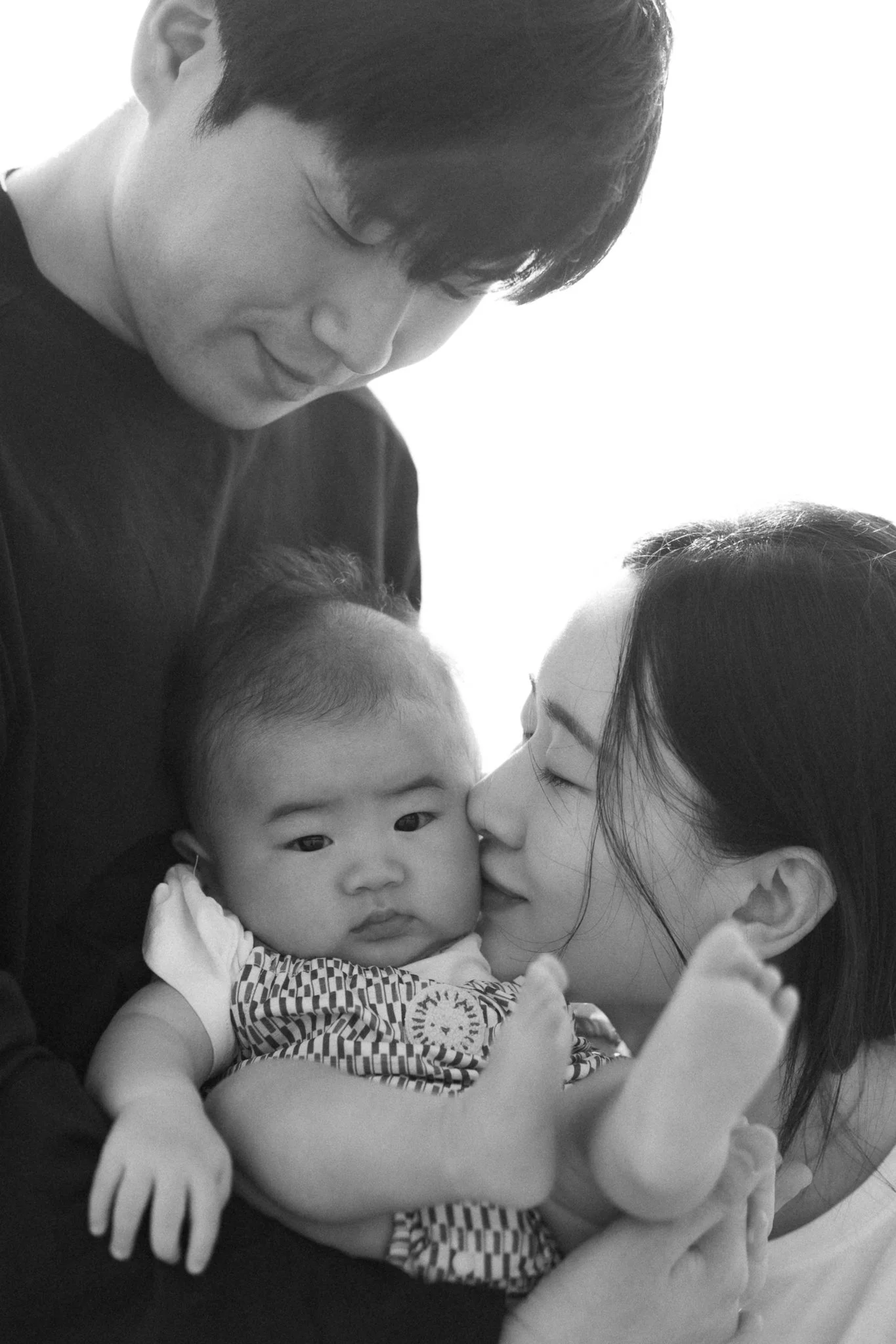 Black and white photo of a man and woman holding a baby, with the woman gently touching her face to the baby's cheek.